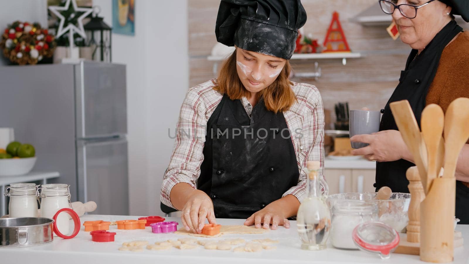 Grandchild choosing cookies shape preparing homemade gingerbread dessert in xmas decorated culinary kitchen. Happy family wearing aprons celebrating christmas tradition enjoying winter holiday