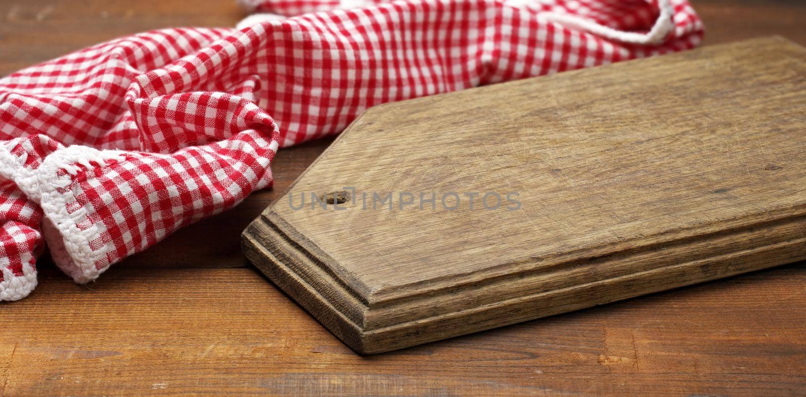 old wooden cutting board and folded red and white cotton kitchen napkin on a wooden brown background, top view by ndanko