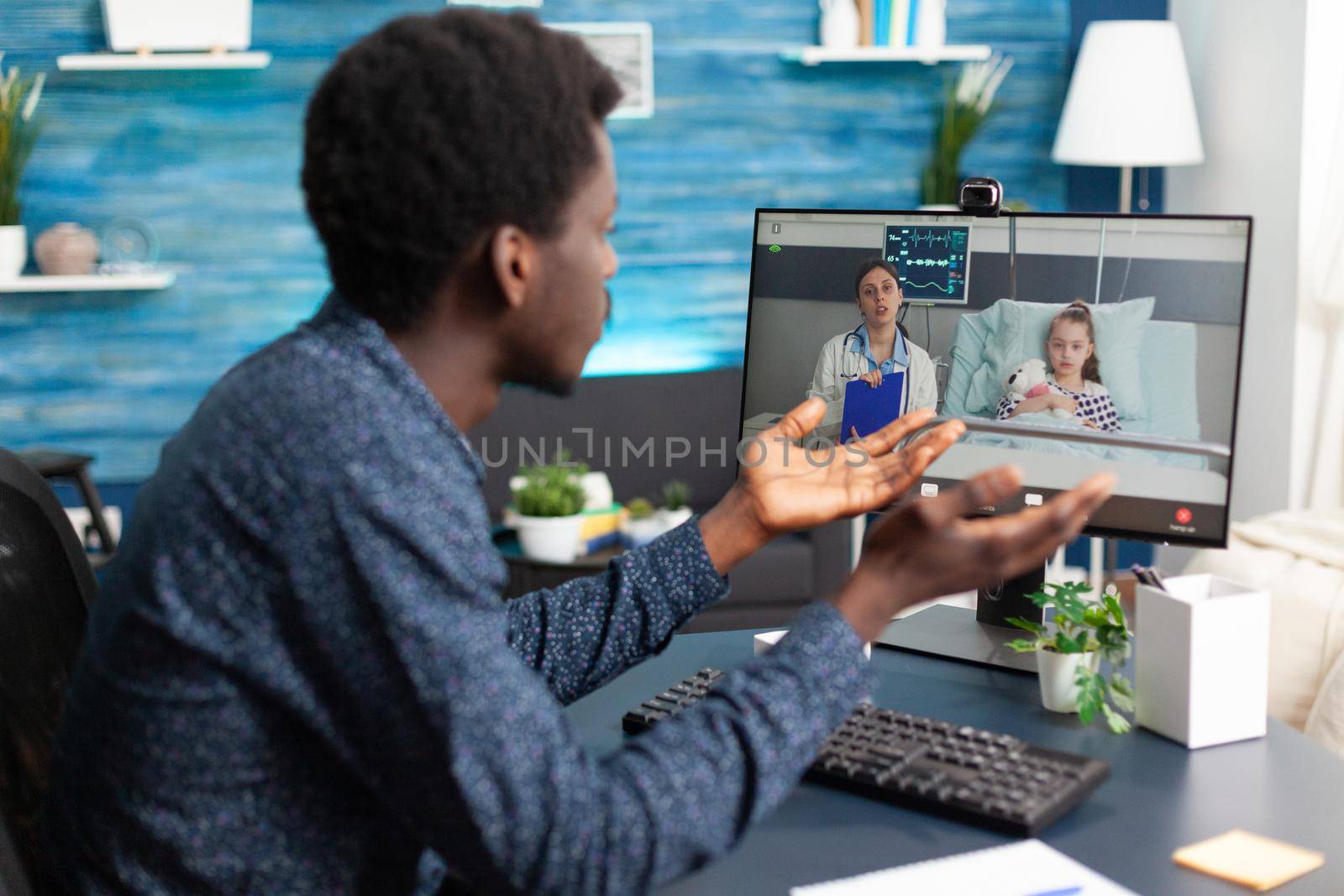 Worried black dad for her little girl in hospital ward talking with doctor on video call using computer webcam for family meeting. Medic consultation via online internet connection