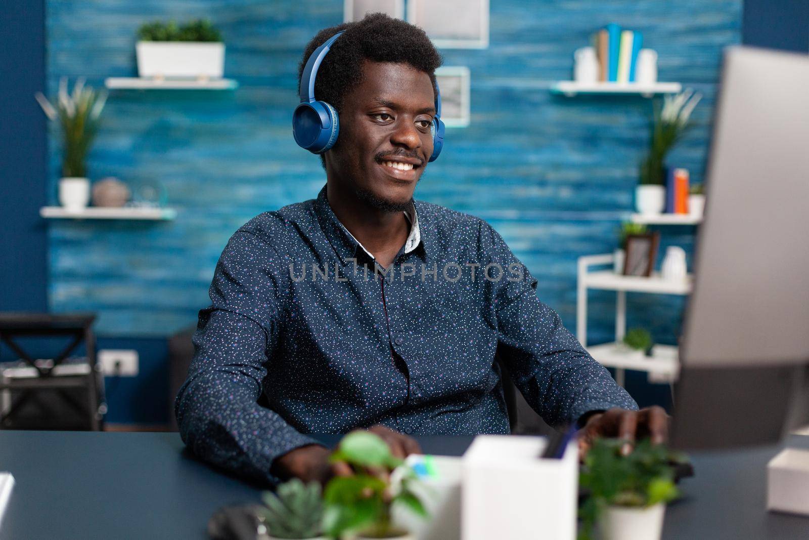 Authentic smiling african american man using laptop and headphones to work from home and learn freelancer webinar or online college courses. Business guy watching movie indoors at desk