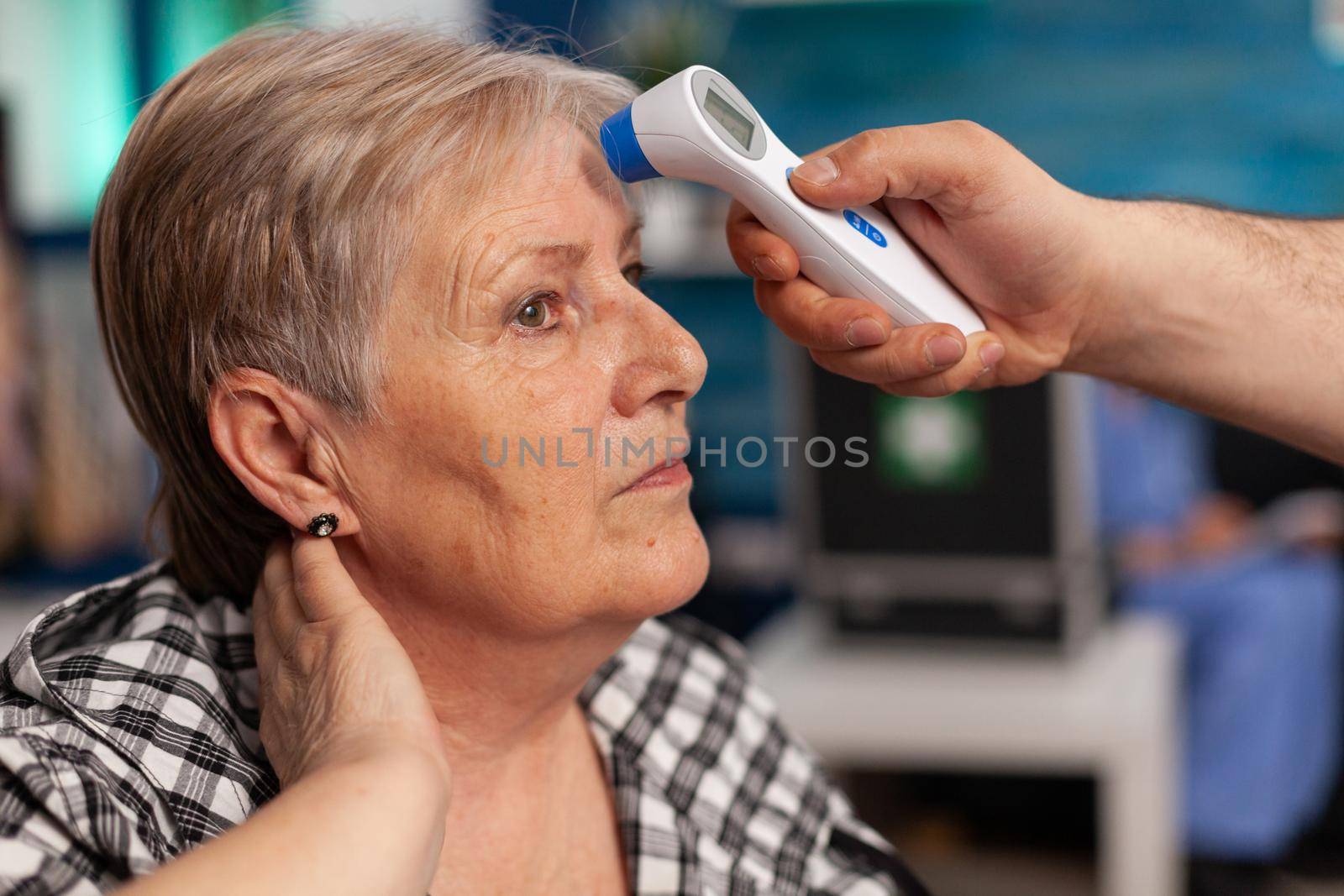 Close-up of assistant man helper checking temperature using medical infrared thermometer discussing with senior woman. Social services nursing elderly retired female. Healthcare assistance