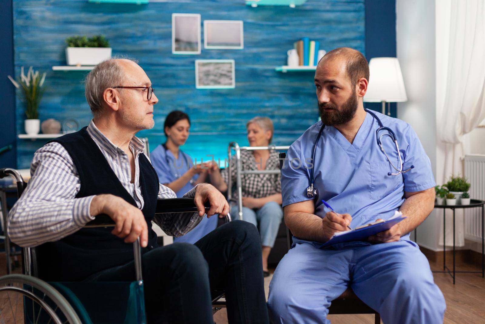 Support assistant man worker writing medication treatment on clipboard discussing with disabled senior male patient during assistance healthcare service. Social services nursing at home