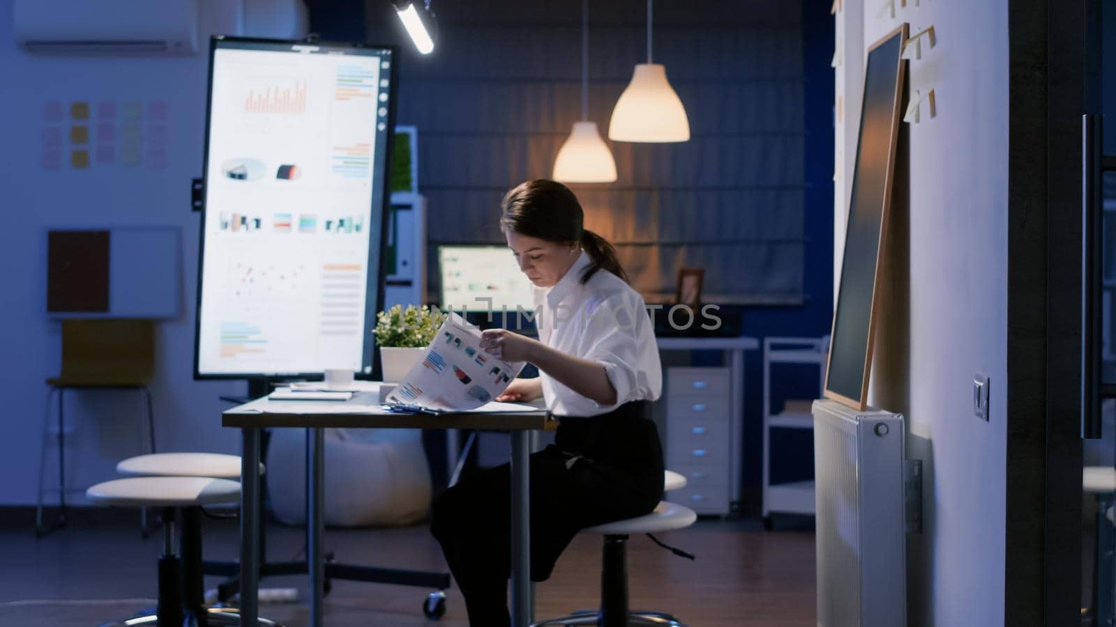 Entrepreneur businesswoman entering in office meeting room late at night sitting at conference table late at night. Focused executive manager woman analyzing company profit documents paperwork