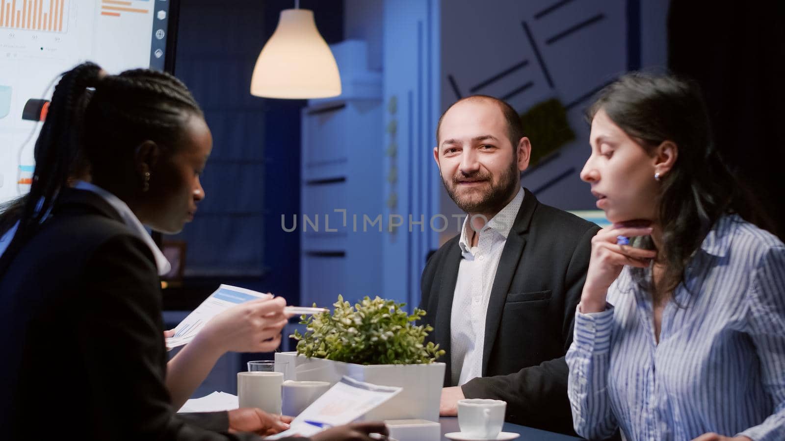 Portrait of smiling manager man looking into camera working at company strategy in meeting office room late at night. Diverse multi-ethnic business teamwork brainstorming management expertise