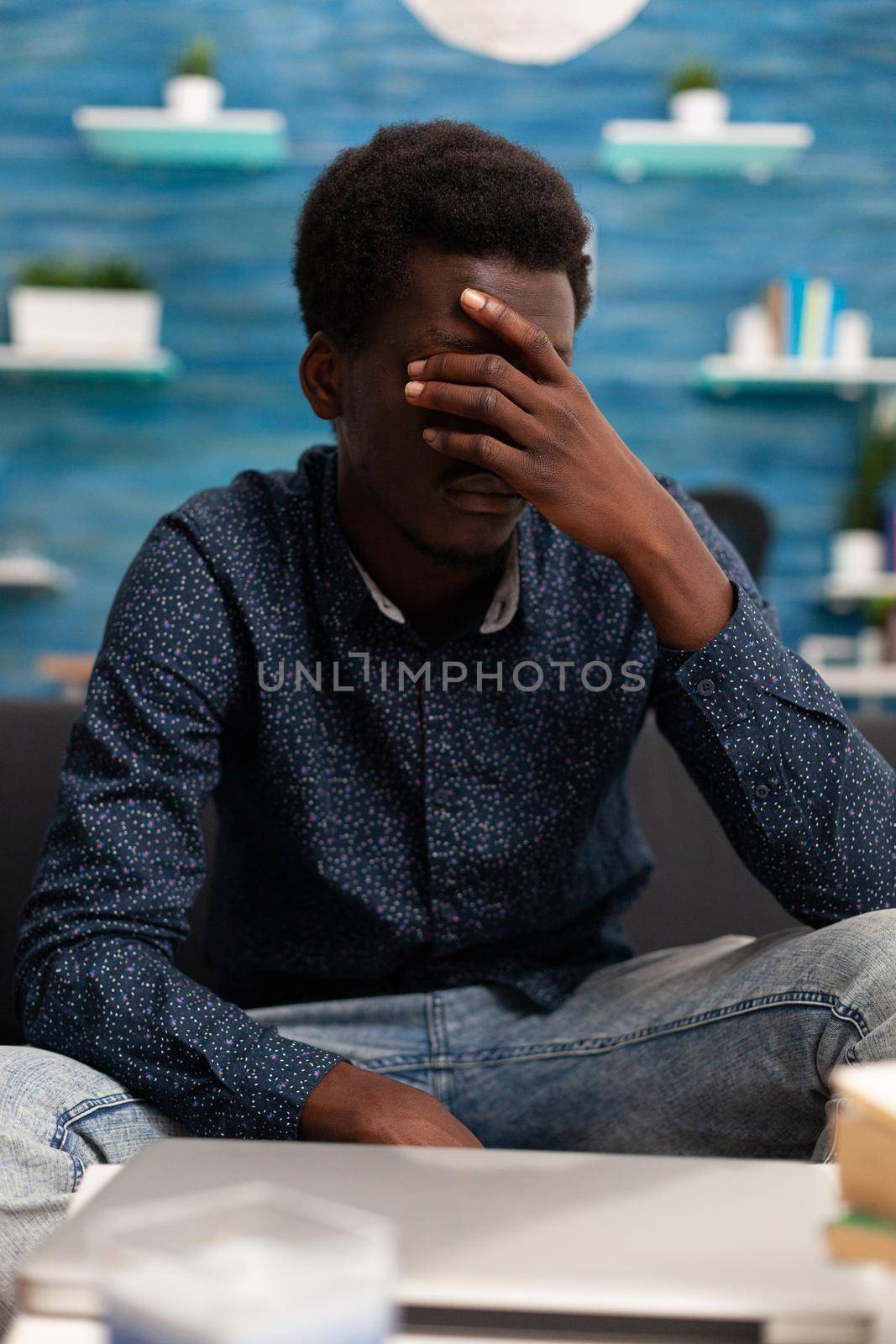 Portrait of stressed, pensive african american man looking out the window thinking about business problems. Adult man in living room working from home office desk. Serious black person