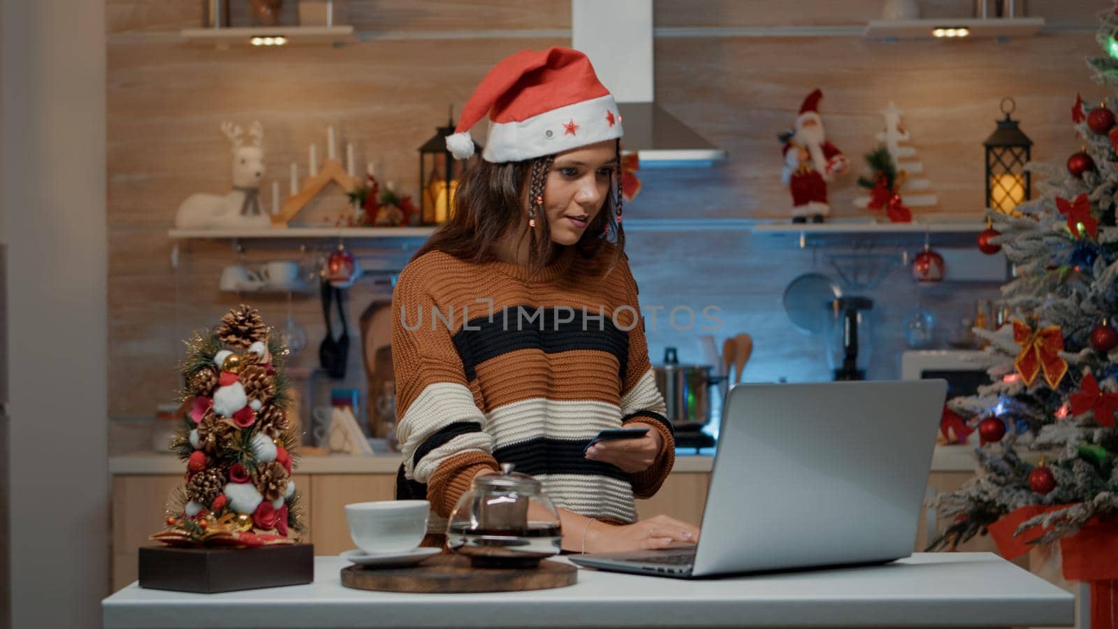 Woman typing credit card information on laptop for buying christmas gifts online. Caucasian young adult doing shopping on internet for festive celebration dinner with friends and family.