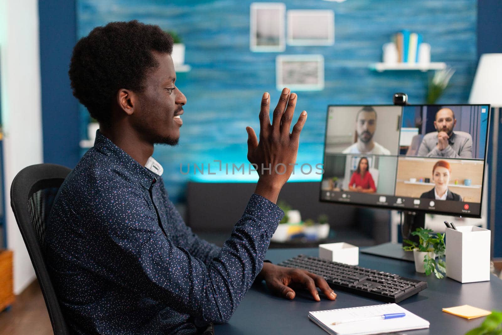 Black man waving to colleagues on video call chat using online internet and webcam communication. Remote worker working from home keeping distance while using technology and computer