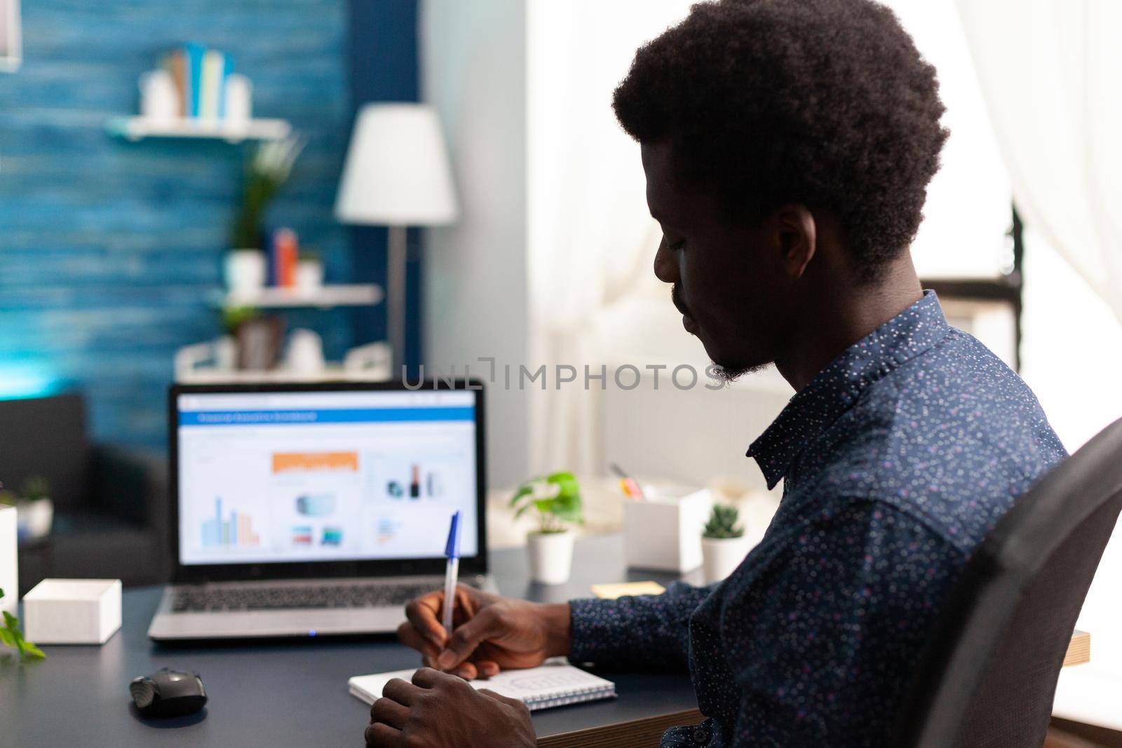 Black man working from home using financial economy data app on laptop. African american guy computer user using business workplace internet online website communication job lifestyle