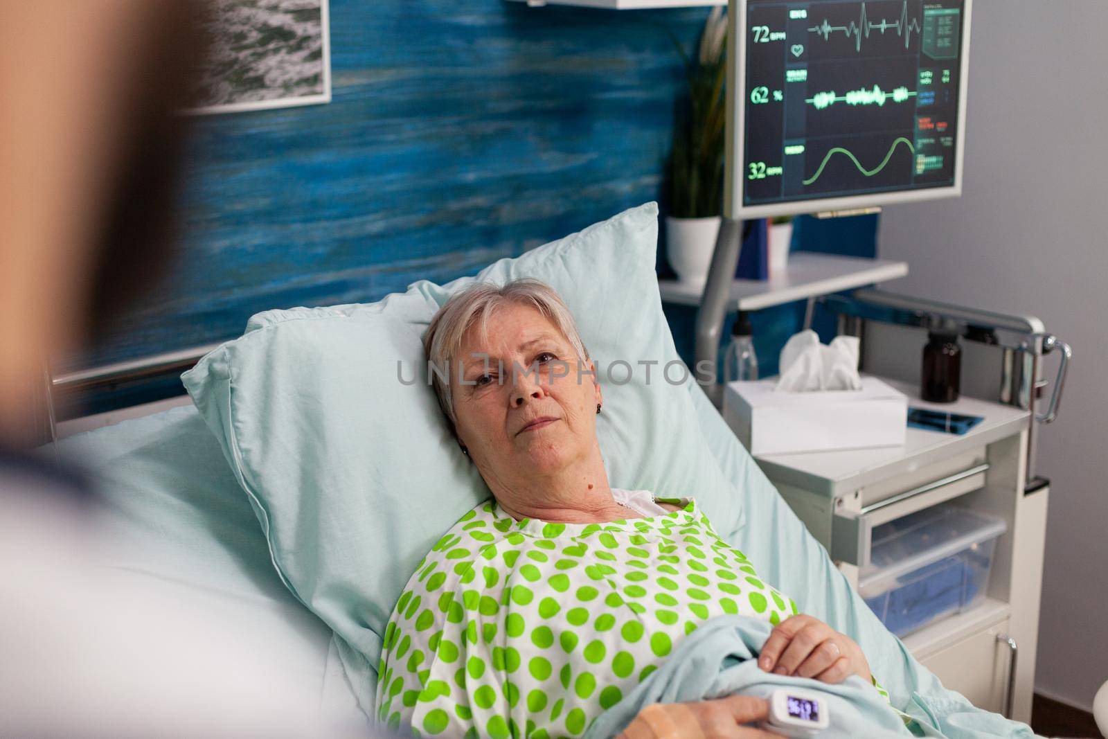 Disabled pensioner woman lying in bed discussing medical treatment with man assistant caregiver during healthcare recovery. Social services nursing elderly retired female. Healthcare assistance