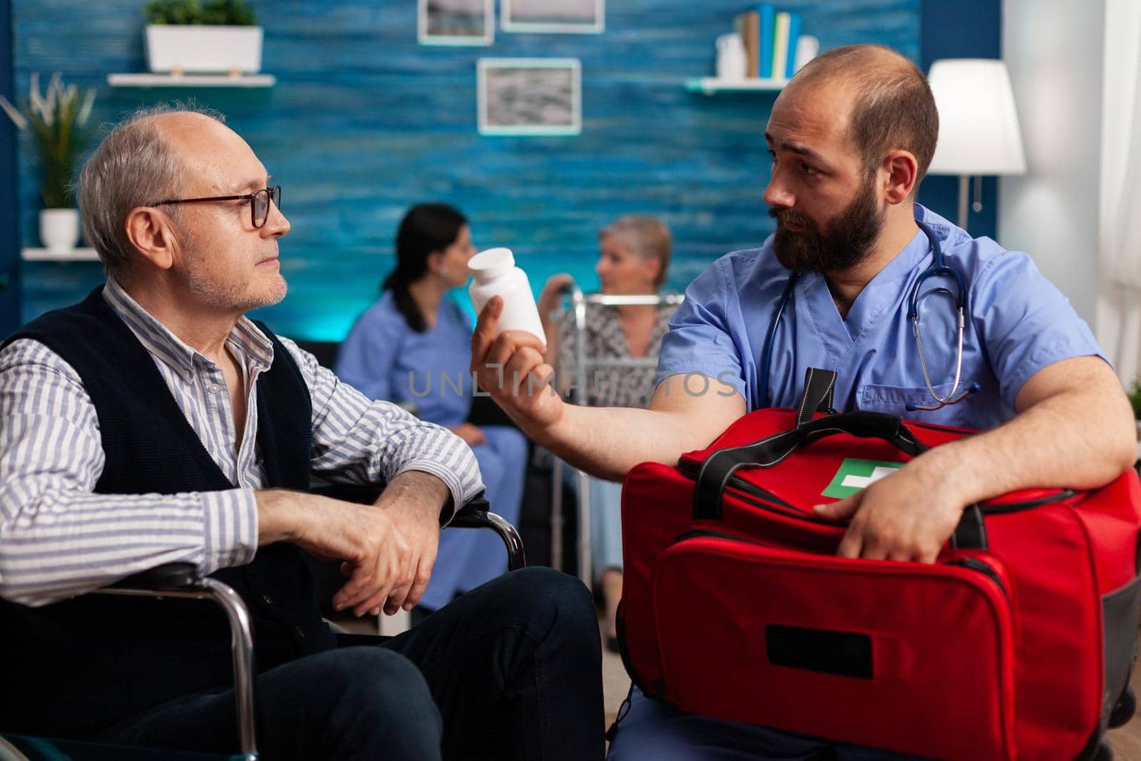 Support nurse worker explaining pills treatment to senior man holding emergency medicine kit bag in hands during therapy. Social services nursing elderly retired male. Healthcare assistance