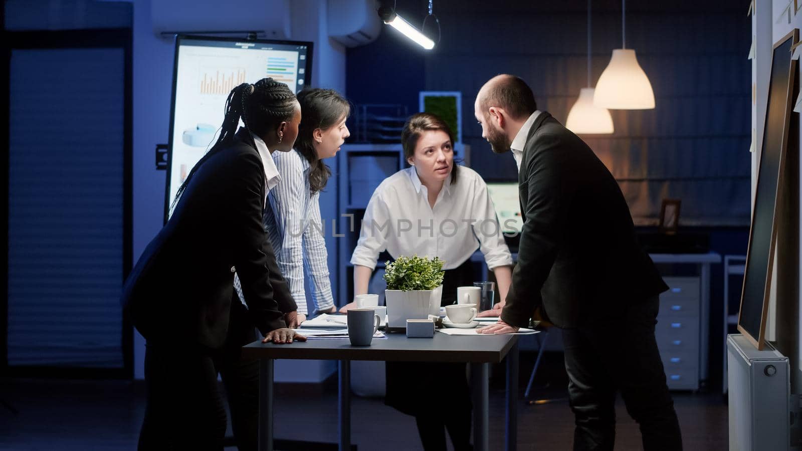 Diverse multi ethnic teamwork standing around conference table brainstorming ideas analyzing management paperwork. Focused coworkers planning company business presentation in meeting room