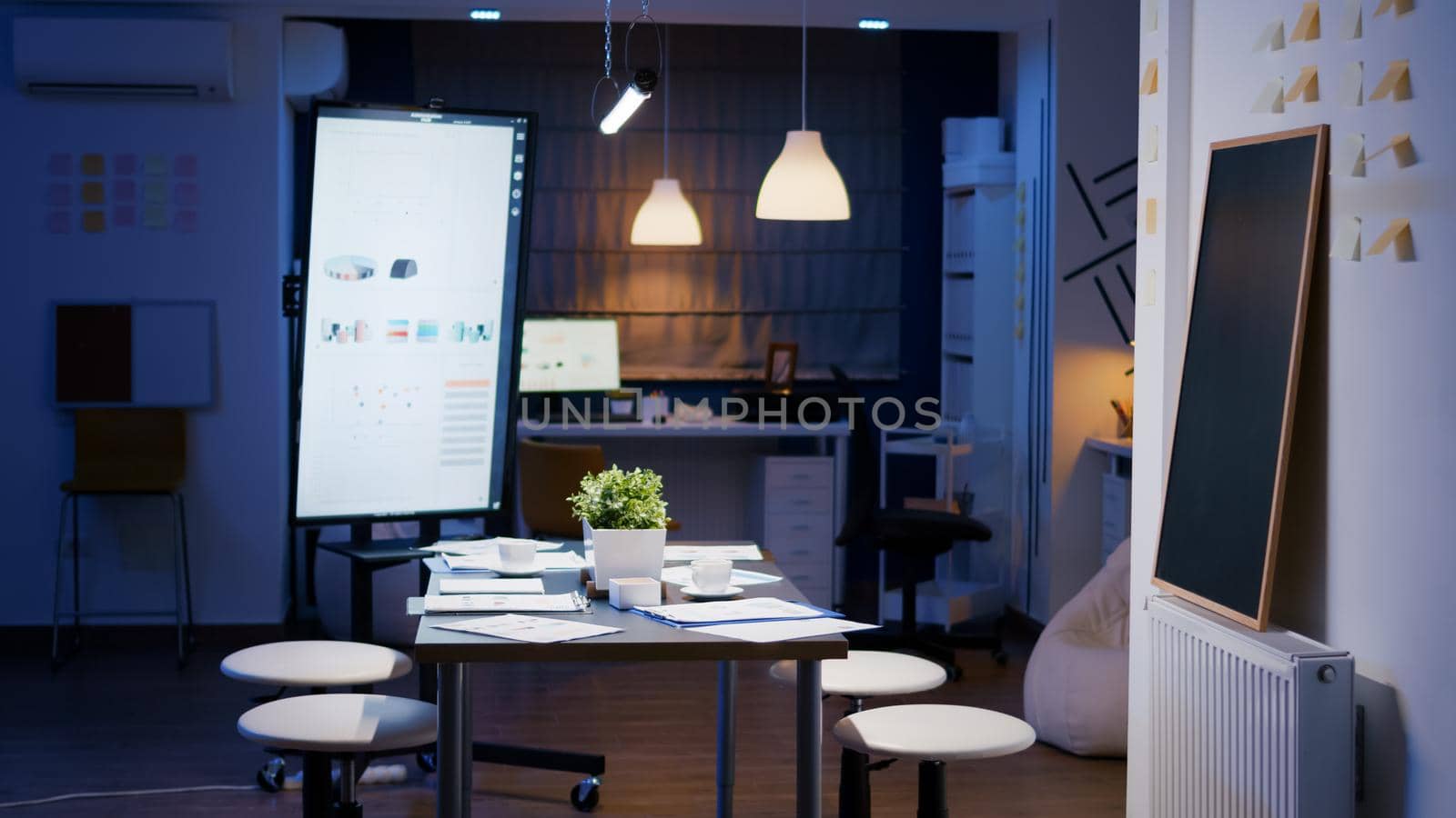 Modern empty business corporate office meeting room is ready for businesspeople late at night. In background on conference table standing company financial documents with economy graphs