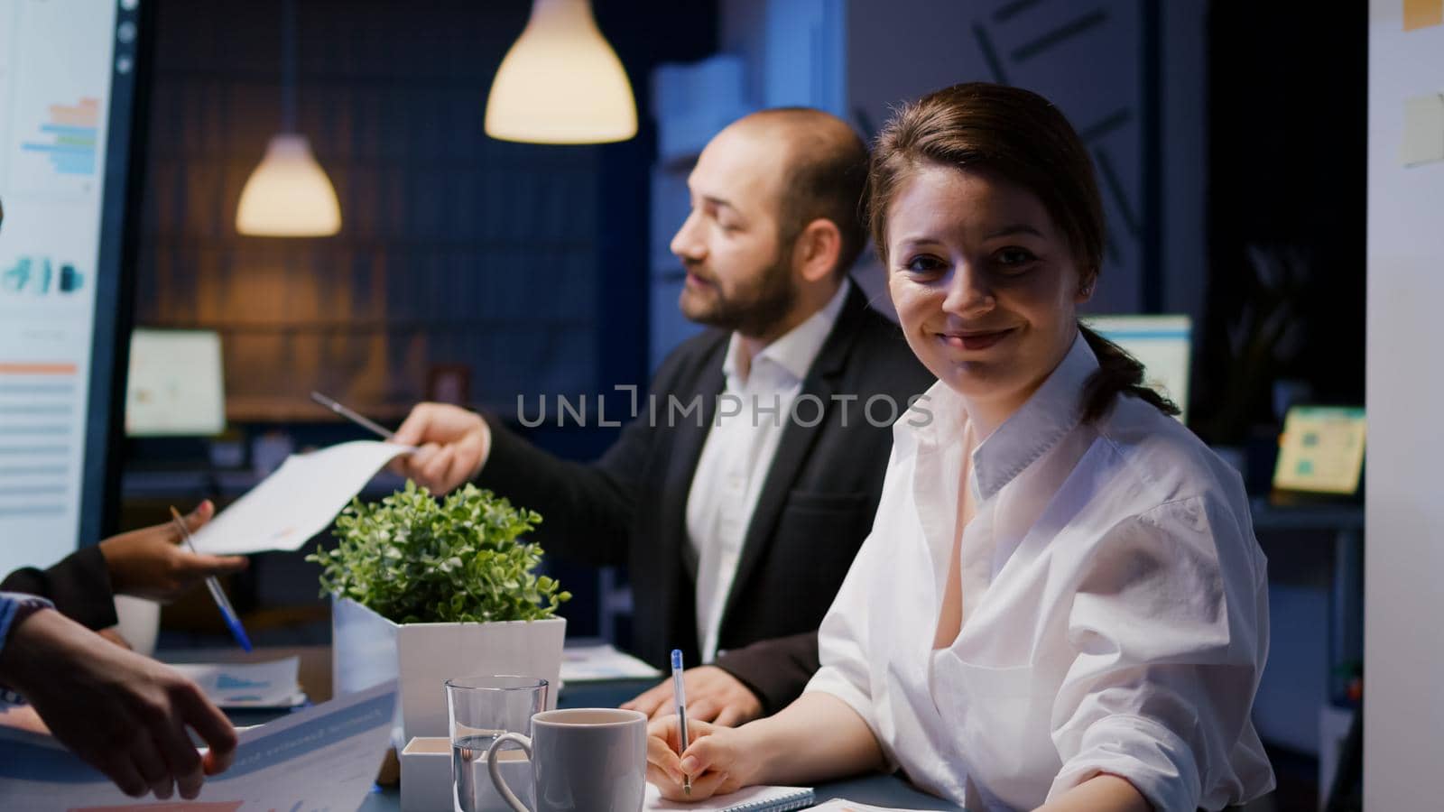 Portrait of smiling businesswoman looking into camera working overtime in business company meeting office by DCStudio