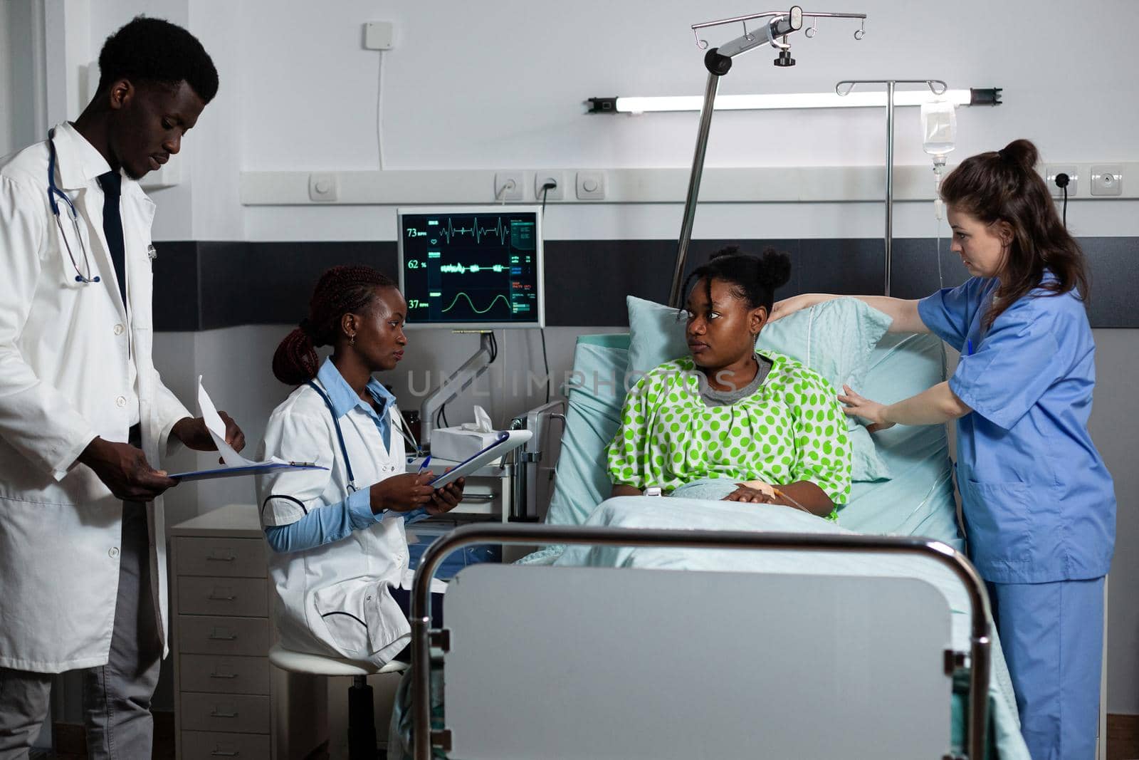 Multi ethnic medical team consulting young person in hospital ward by DCStudio