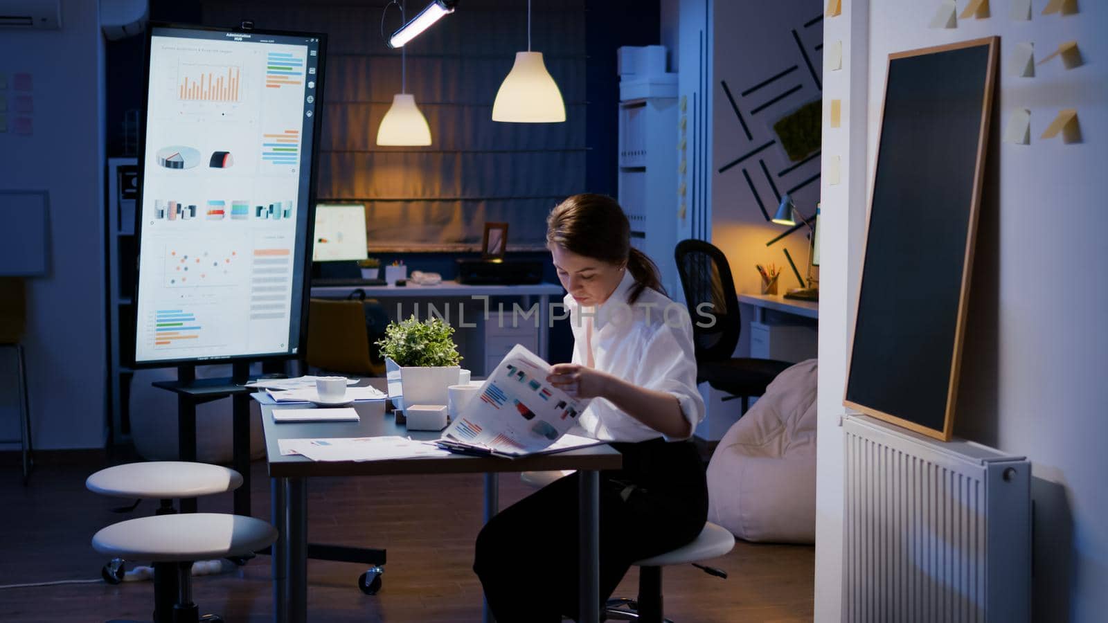 Businesswoman enter in company office meeting room late at night sitting at desk late at night by DCStudio