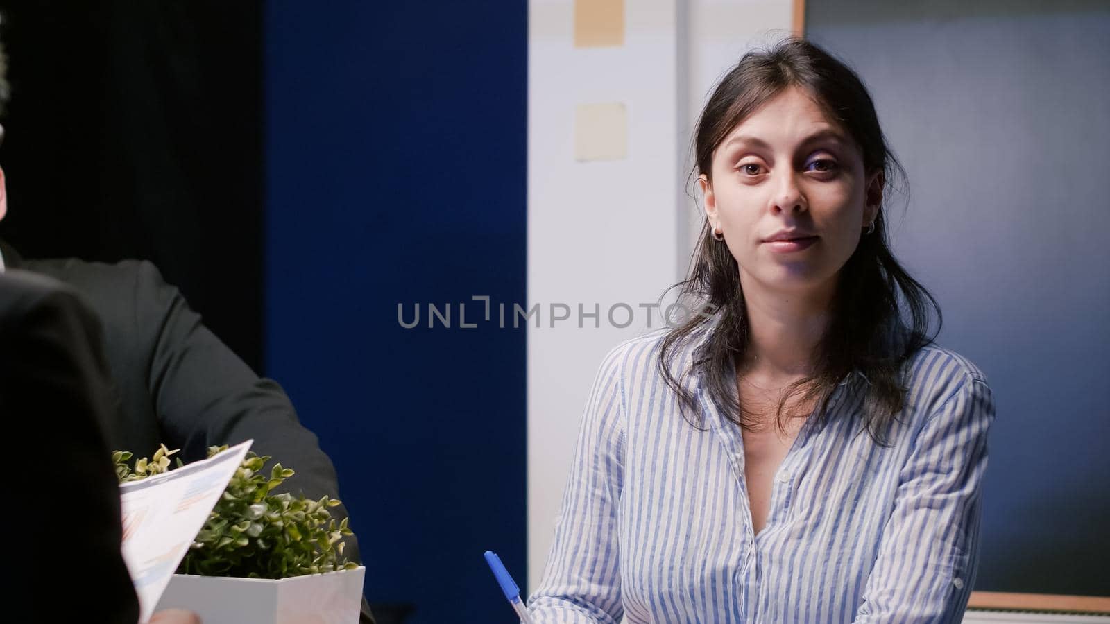 Portrait of smiling businesswoman looking into camera while sitting at conference table in company meeting office room. Multi-ethnic teamwork discussing company investment expertise late at night