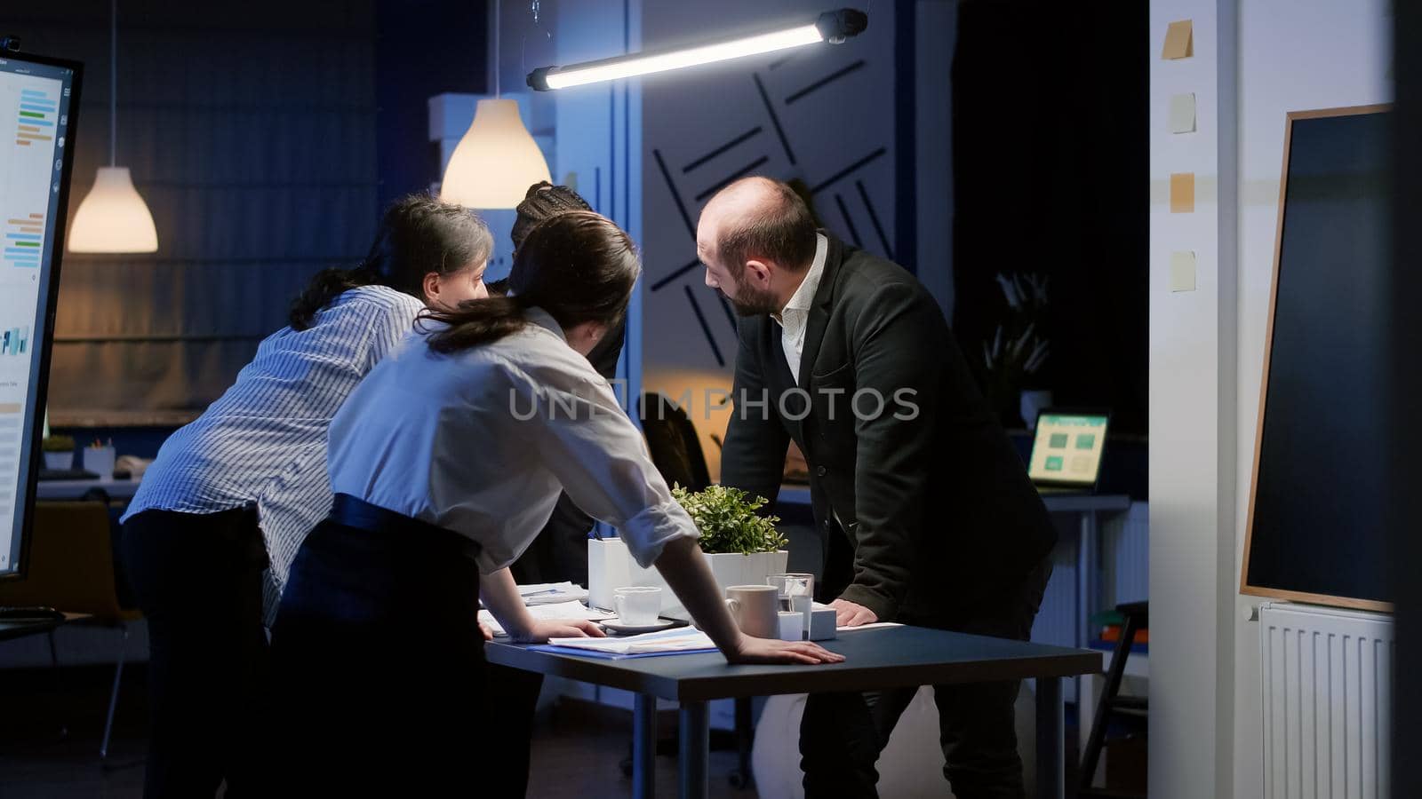 Diverse business teamwork standing at conference table checking management graphs paperwork by DCStudio