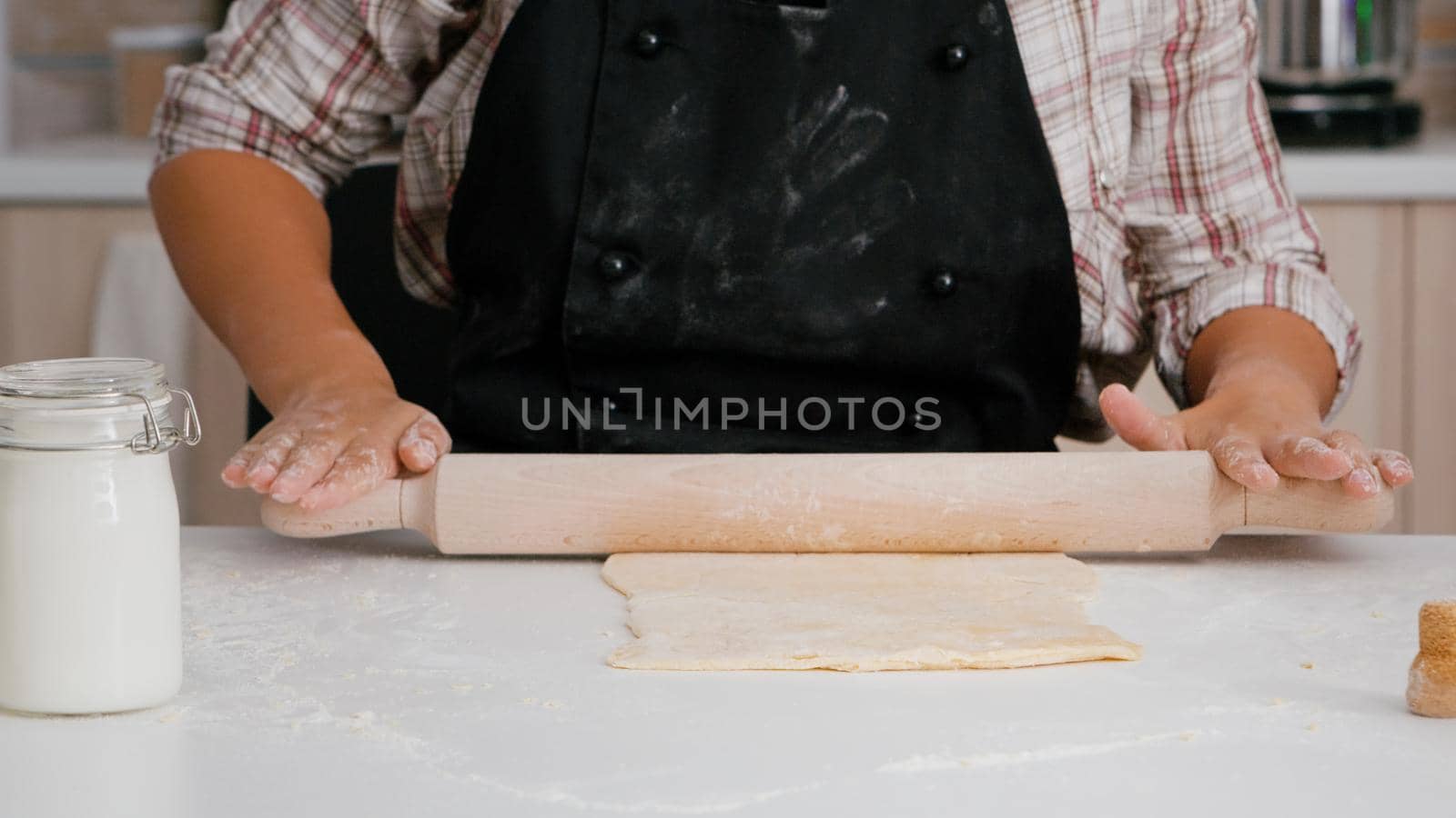 Closeup of child hands preparing homemade dough using rolling pin cooking xmas traditional delicious cookies in culinary kitchen. Girl enjoying christmas holiday standing at table in culinary kitchen