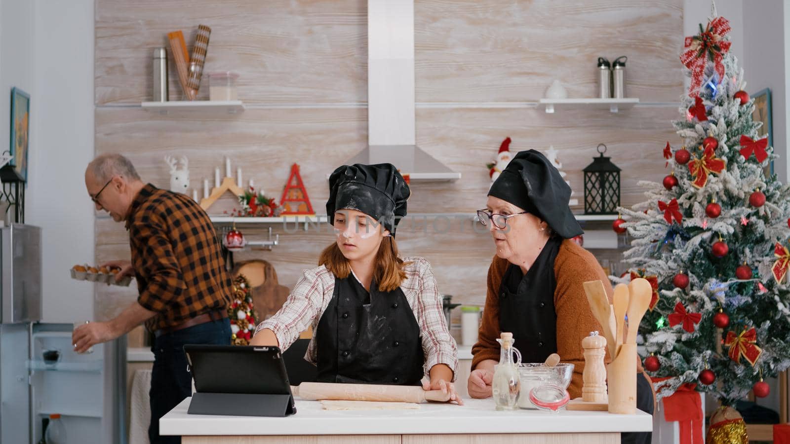 Happy granddaughter preparing gingerbread dough using rolling pin by DCStudio