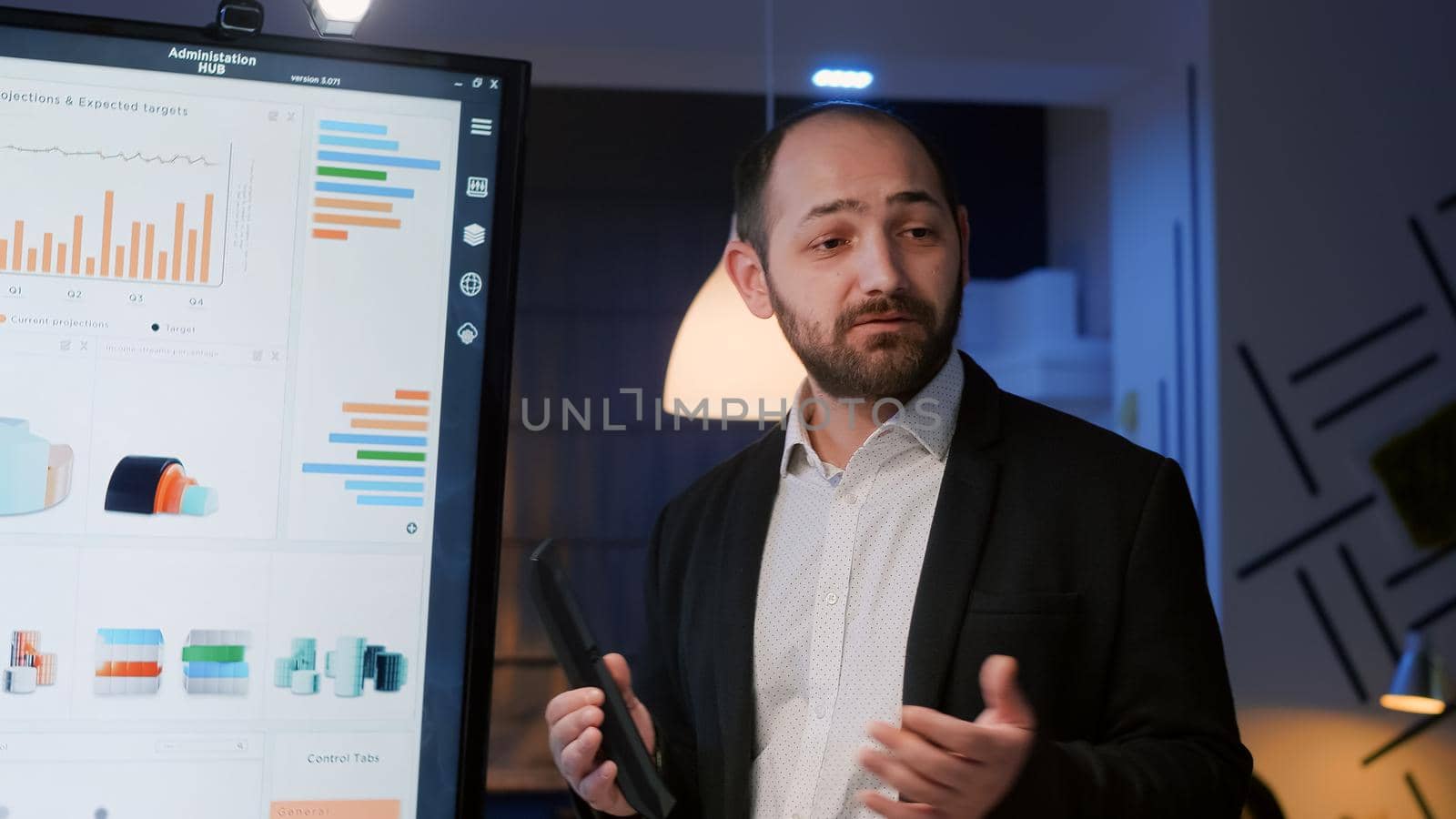 Businessman presenting management statistics using presentation monitor late at night by DCStudio