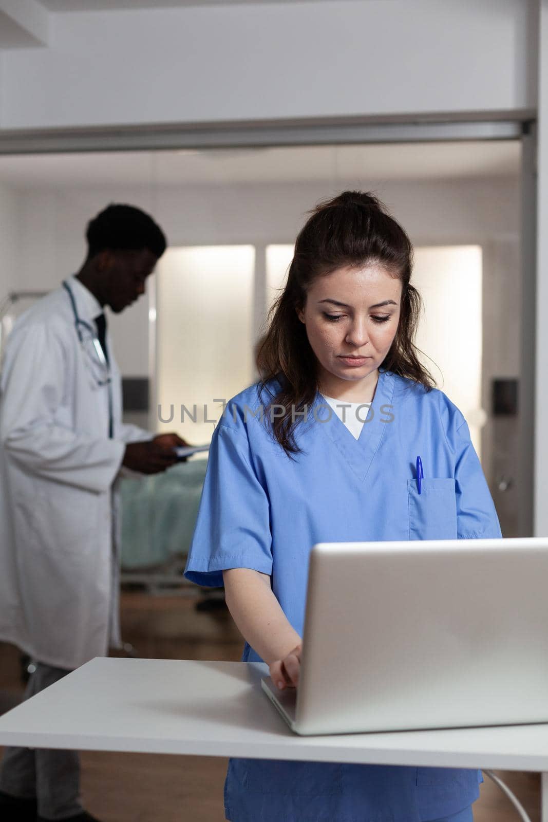 Caucasian woman using laptop at desk in hospital ward for professional healthcare. Young adult with nurse occupation working as consultant for specialist, surgeon, medic, doctor