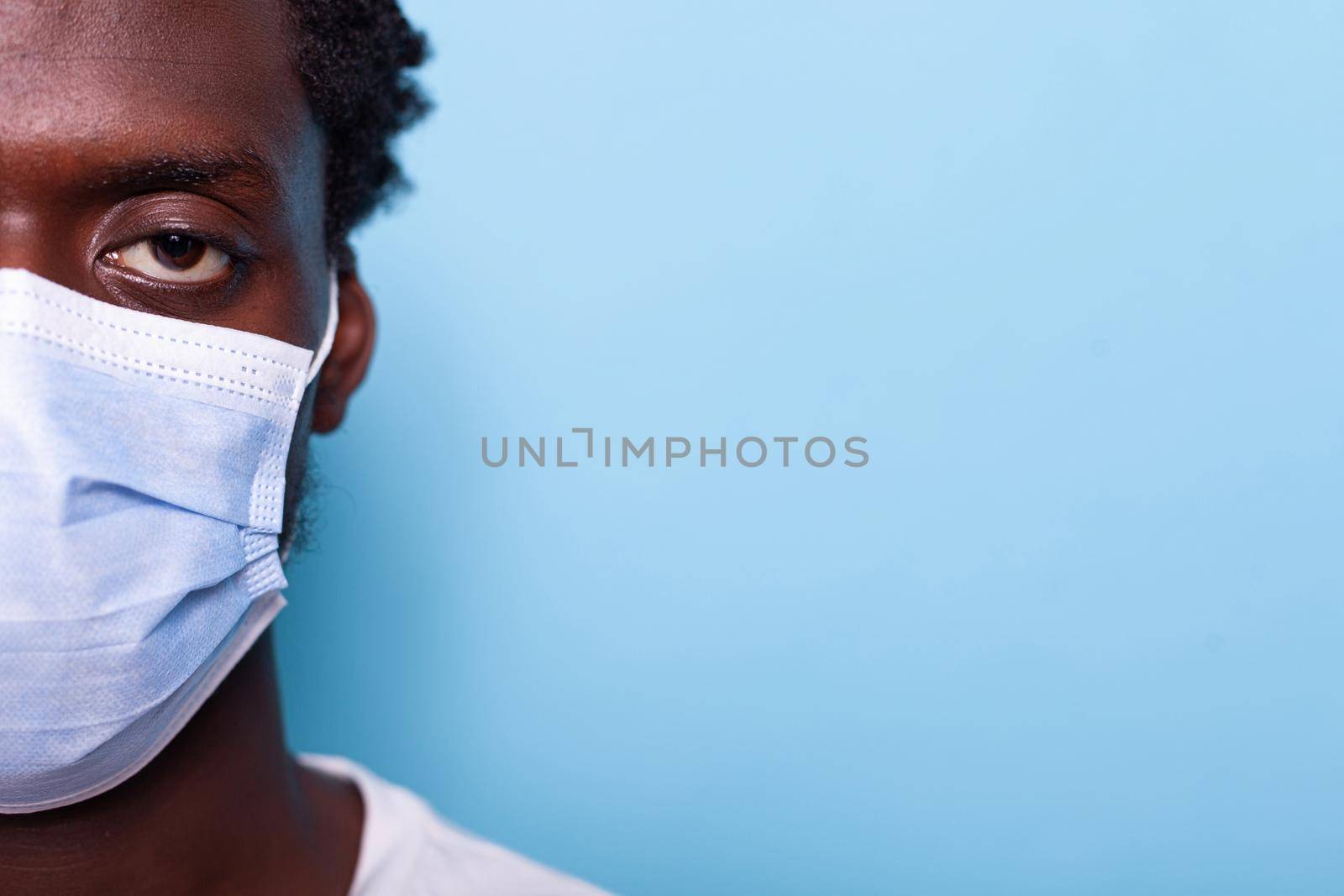 Close up of eye of african american adult wearing face mask while looking at camera in studio. Black face with protection against coronavirus for healthcare, standing over isolated background