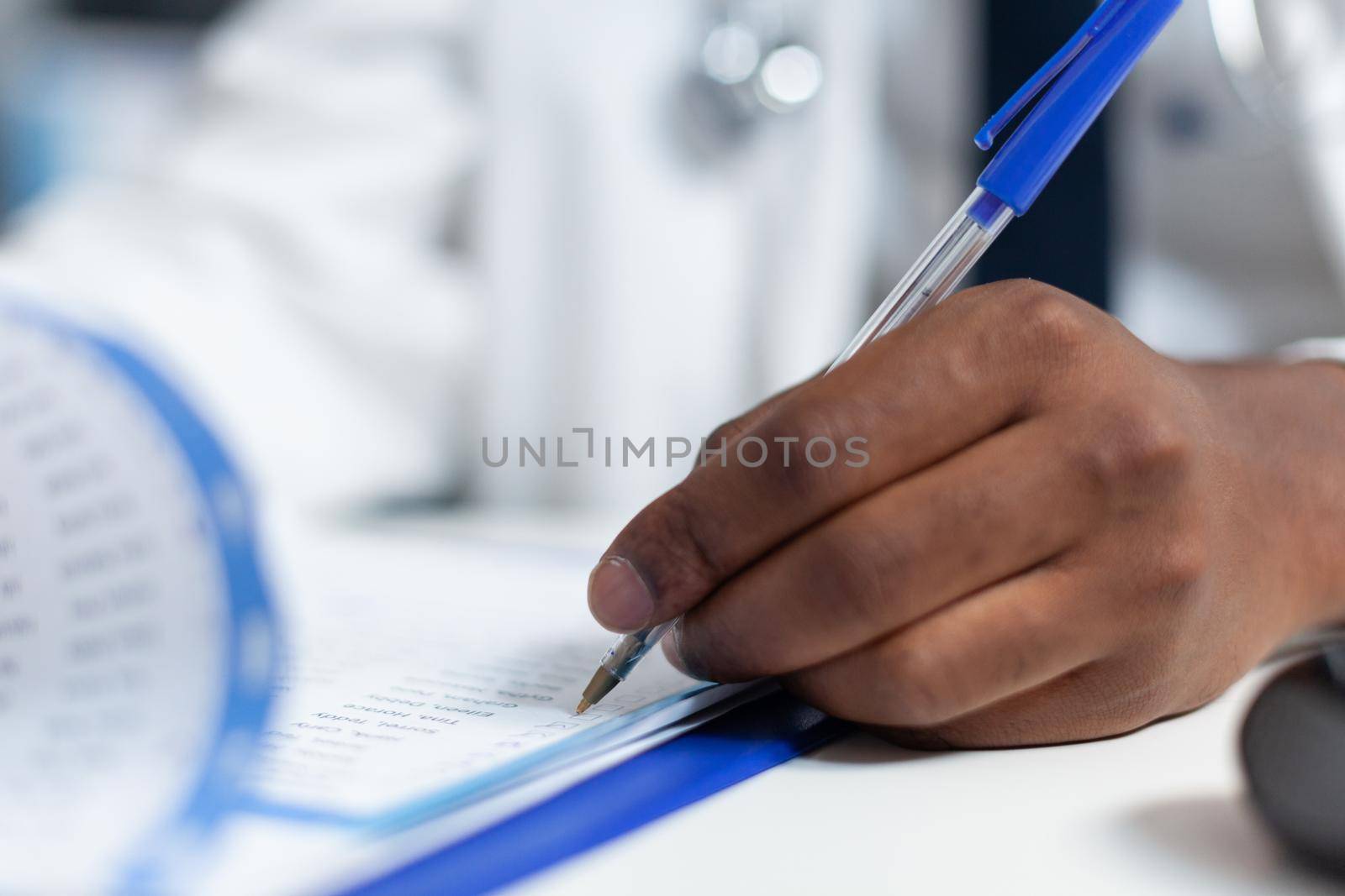 Closeup of african american doctor hand analyzing ill symptoms writing medical treatment on clipboard. Therapist man working at medicine prescription for sick patient in hospital office