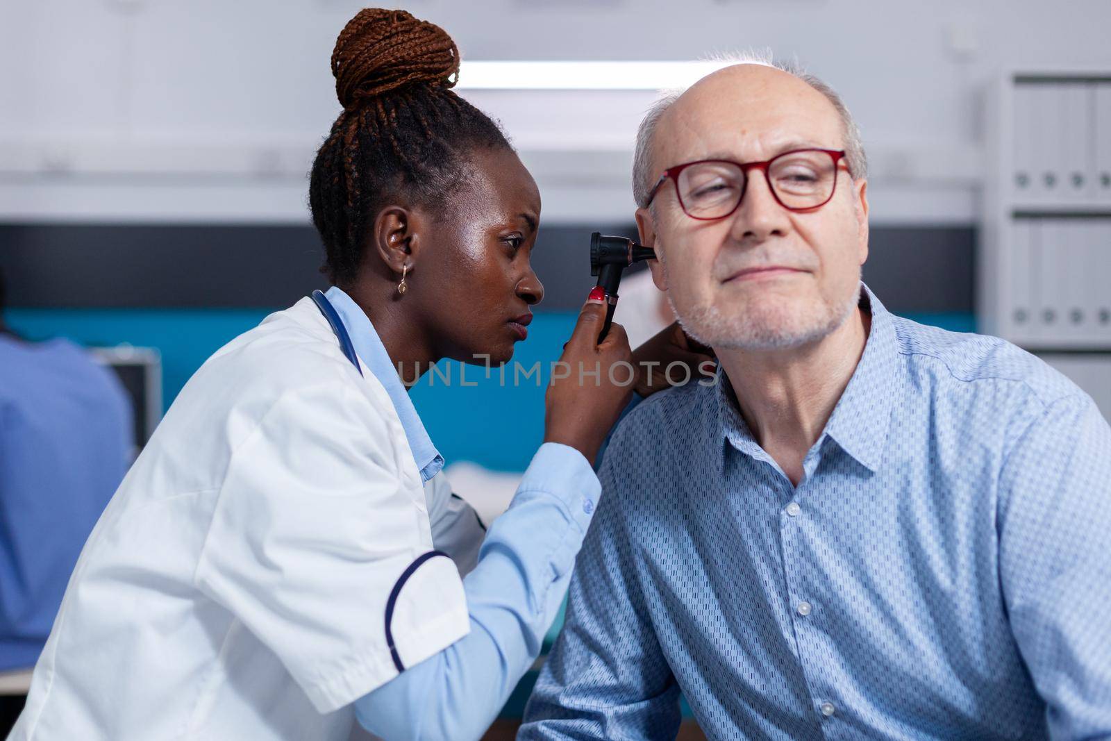 Otologist of african ethnicity consulting elder patient by DCStudio