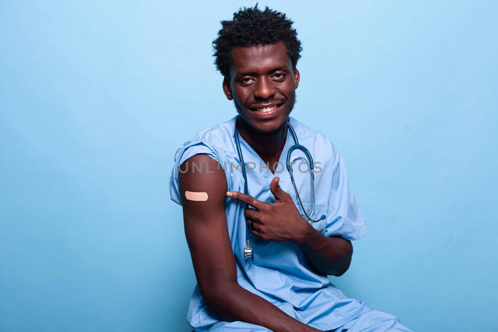 African american nurse pointing to vaccine shot bandage by DCStudio