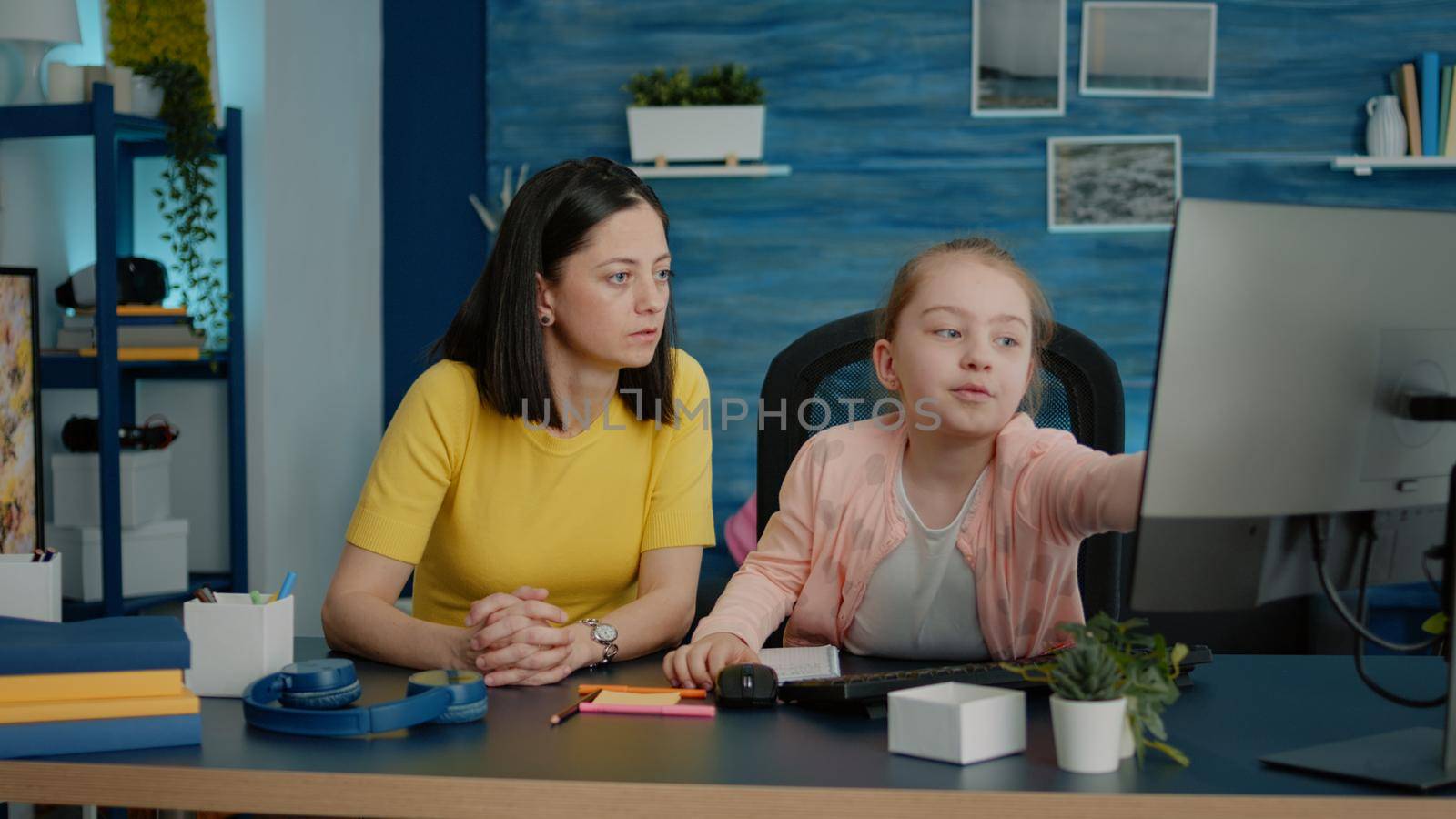 Young girl receiving help with homework from mother. Little child and mother doing school tasks for online remote class lesson at home with computer and notebook. Pupil and parent