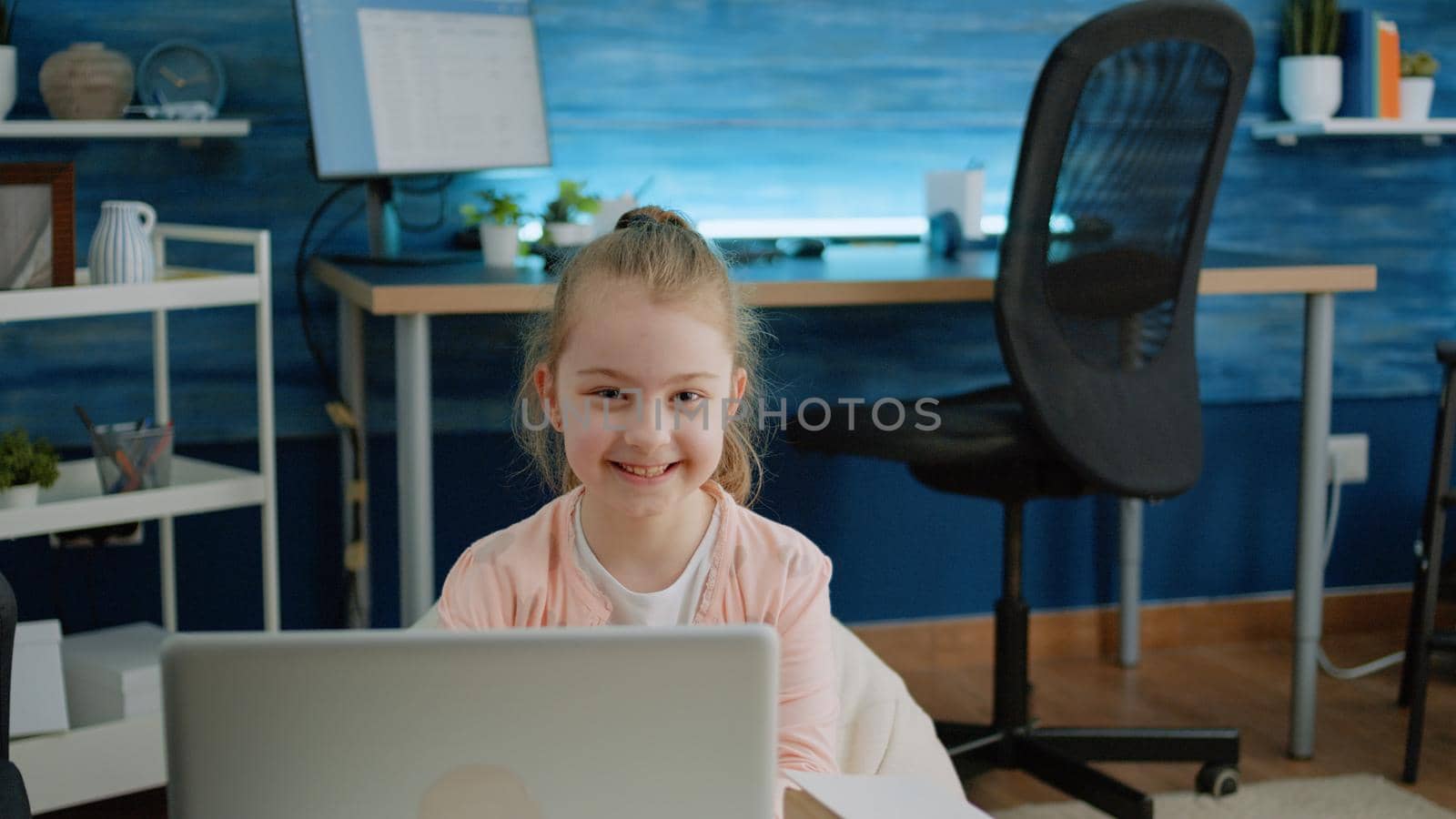 Portrait of young girl smiling and holding laptop at home for homework and online courses. Little child looking at camera and preparing for remote school lessons on modern device