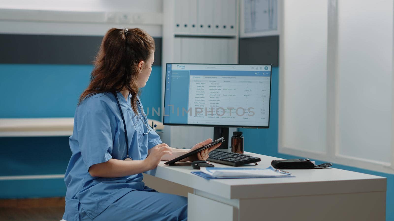 Medical assistant working with computer and digital tablet for healthcare system and appointments. Woman nurse holding device with touch screen in doctors office for annual checkup visit.