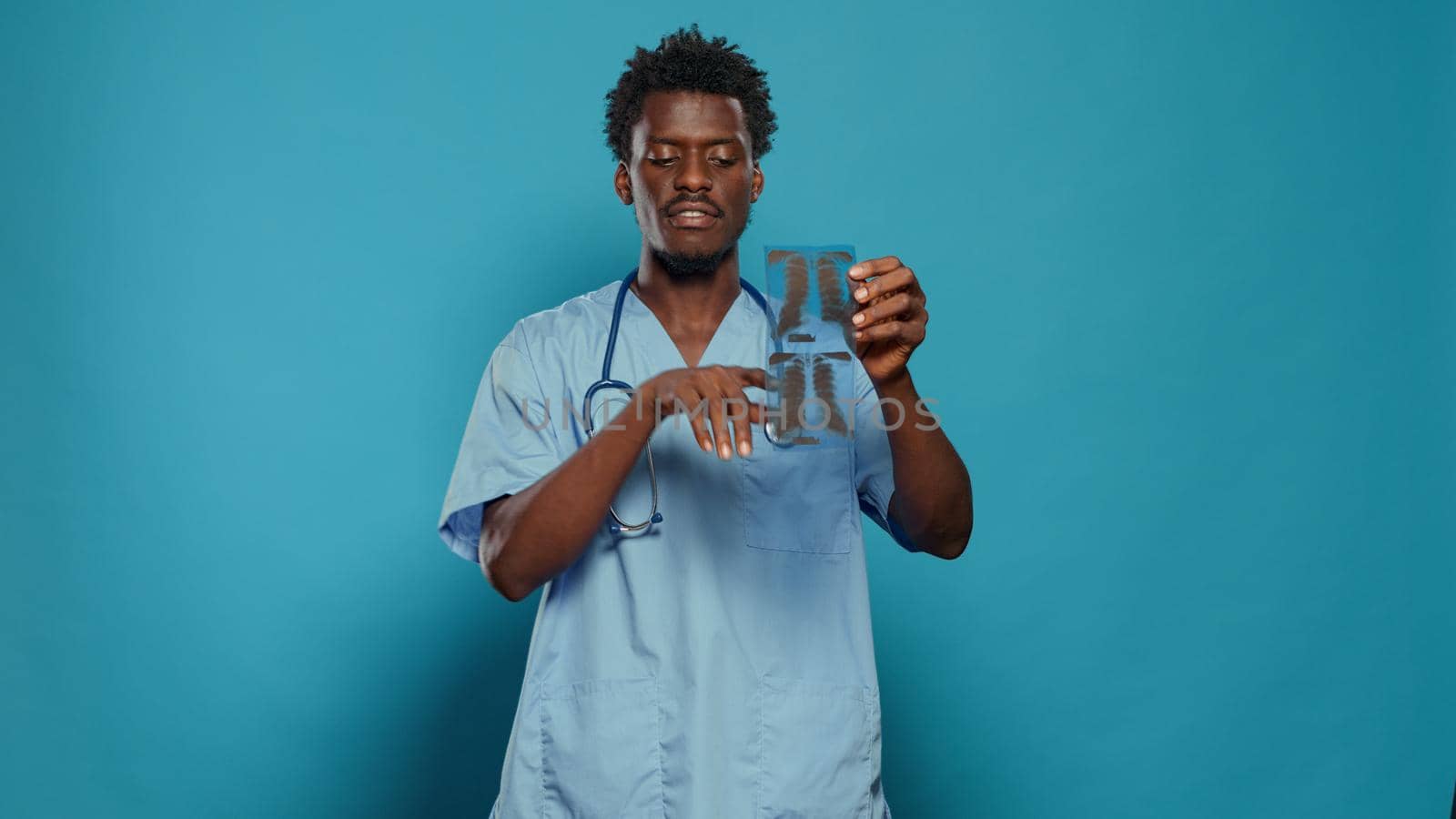 Medical assistant holding x ray scan and explaining disease in studio. Man nurse presenting radiography for diagnosis while wearing uniform and stethoscope for healthcare over background