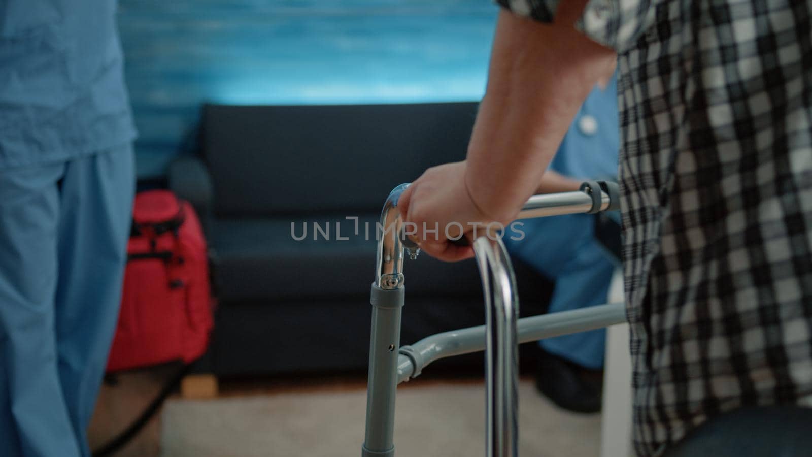 Close up of disabled patient having hand on walk frame while walking for injury recovery in nursing home. Man nurse supporting old woman using object for transportation.