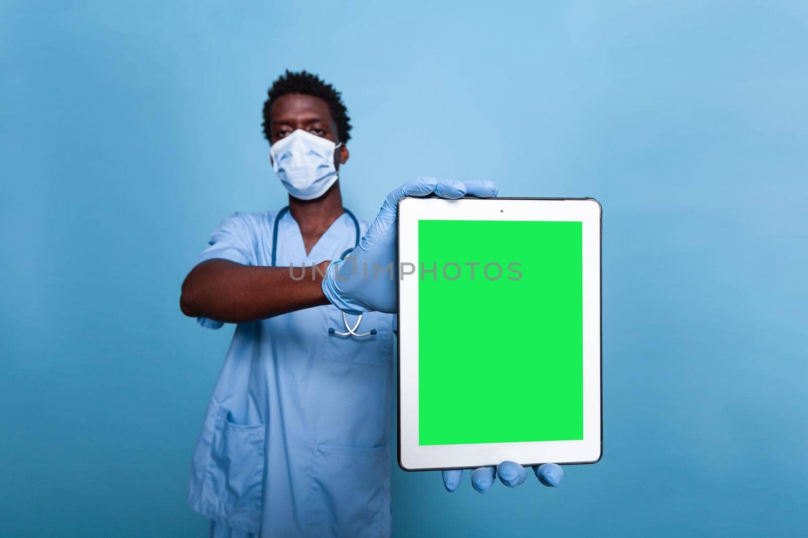 Medical nurse holding vertical green screen on tablet in studio. Healthcare assistant with covid 19 face mask and stethoscope having gadget with chroma key, showing isolated mockup template.