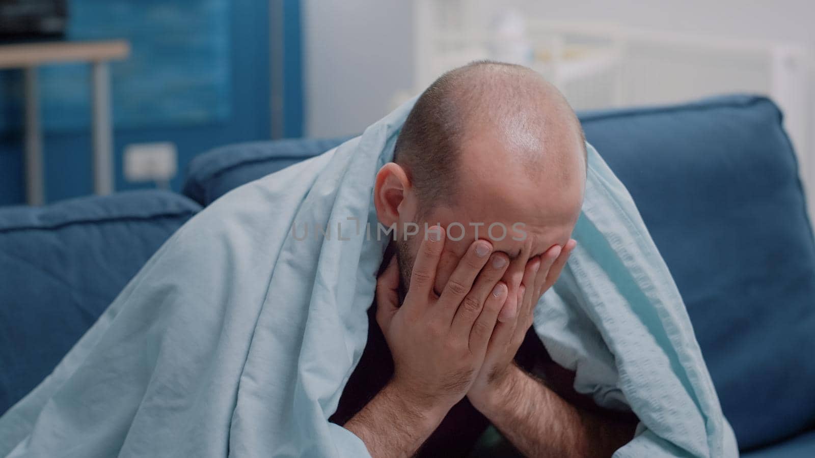 Close up of sick person rubbing temples against headache feeling miserable because of disease. Unwell man with migraine and virus symptoms while holding hands on head in blanket.