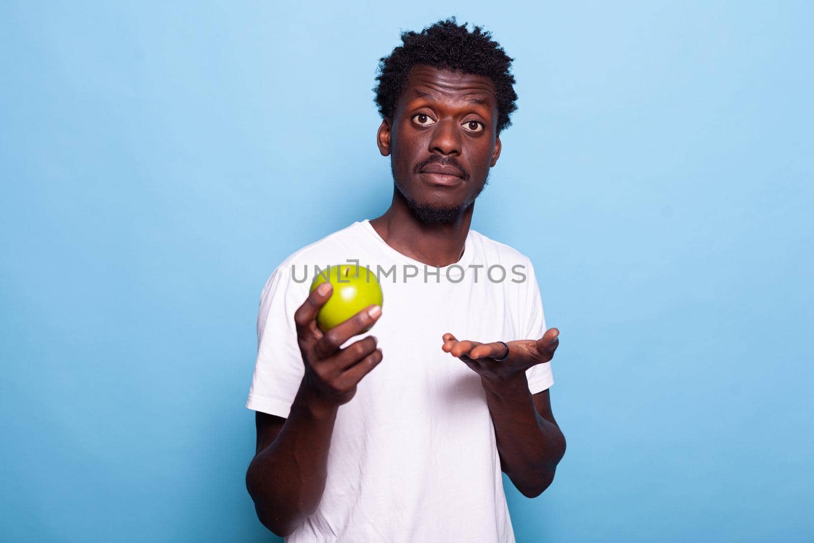 Young adult showing green apple to camera in studio by DCStudio