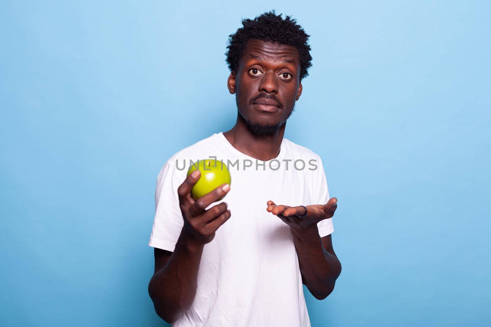 Young adult showing green apple to camera in studio. Portrait of person holding raw fruit with natural vitamins for organic lifestyle. Cheerful man with healthy nutrition and fresh diet