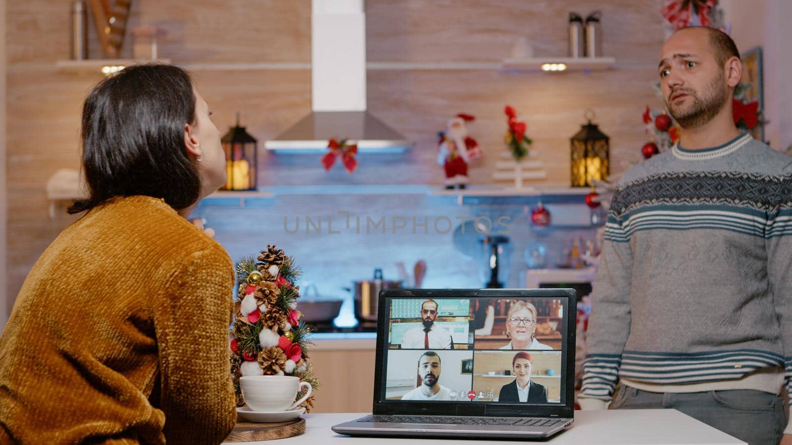 Woman using video call for work meeting on christmas eve while man waiting for holiday celebration at home. Businesswoman working on christmas, couple delaying winter festivity.