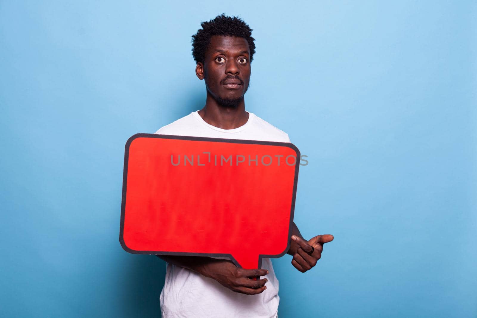 African american man holding red speech bubble in studio. Black adult with blank sign for communication and conversation on board looking at camera and standing over isolated background