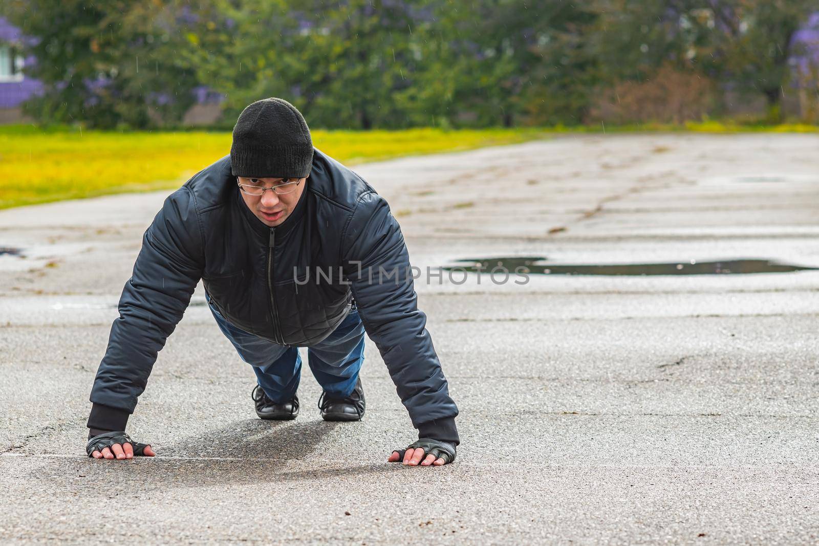 A man performs a classic pectoral exercise outdoors in the rain in the fall. The athlete does push-ups to maintain muscle tone