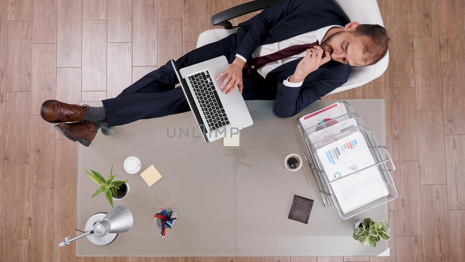 Top view of businessman in suit keeping his feet on desk while typing company statistics on laptop. Executive manager working at financial strategy analyzing management profit in startup office