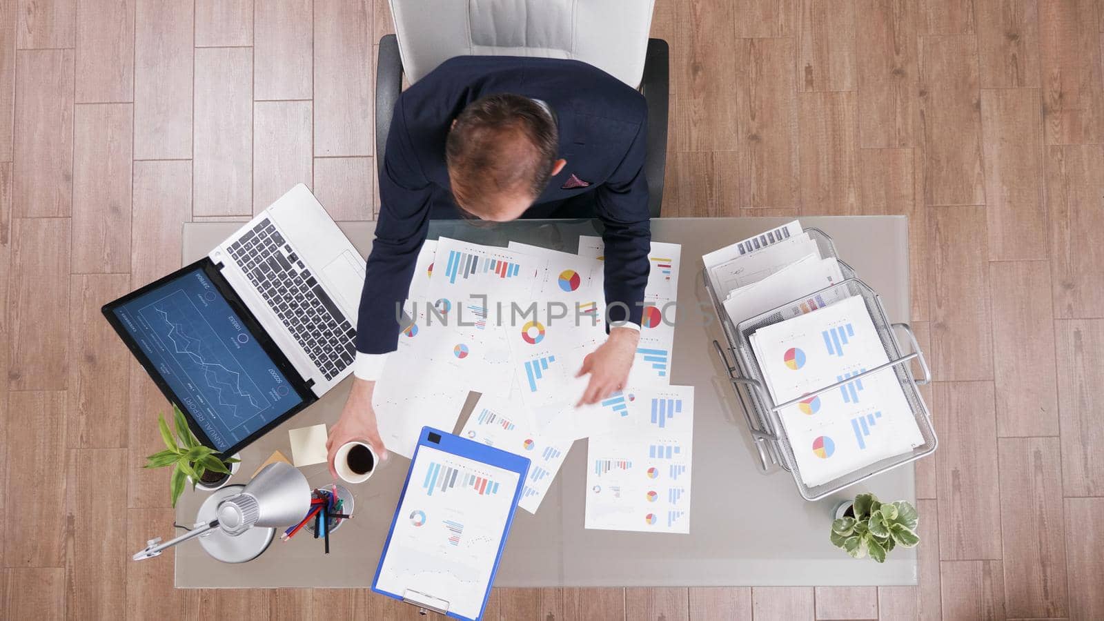 Top view of businessman holding cup of coffee while typing company statistics working at management strategy in startup office. Executive manager in suit analyzing investments documents on computer