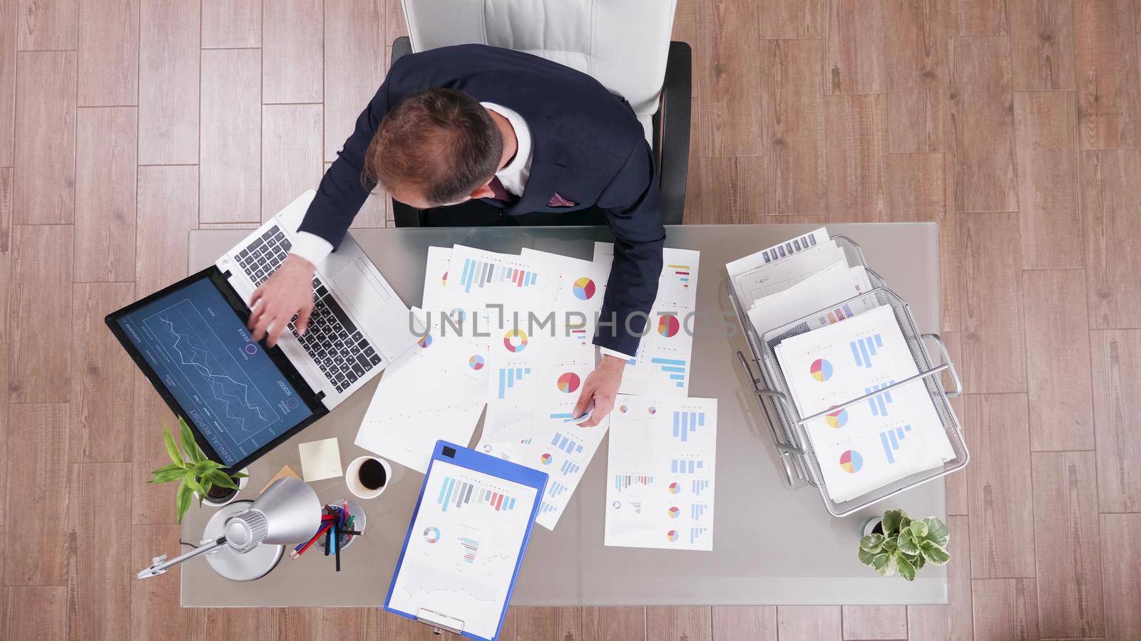 Top view of businessman typing company startegy on laptop computer while working at management investments project in startup office. Manager in suit analyzing management statistics