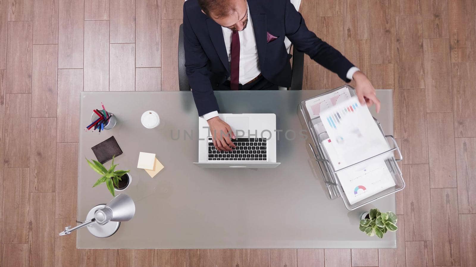 Top view businessman typing management strategy on laptop while reading data from business chart paperwork. Executive manager working at company investments in startup office