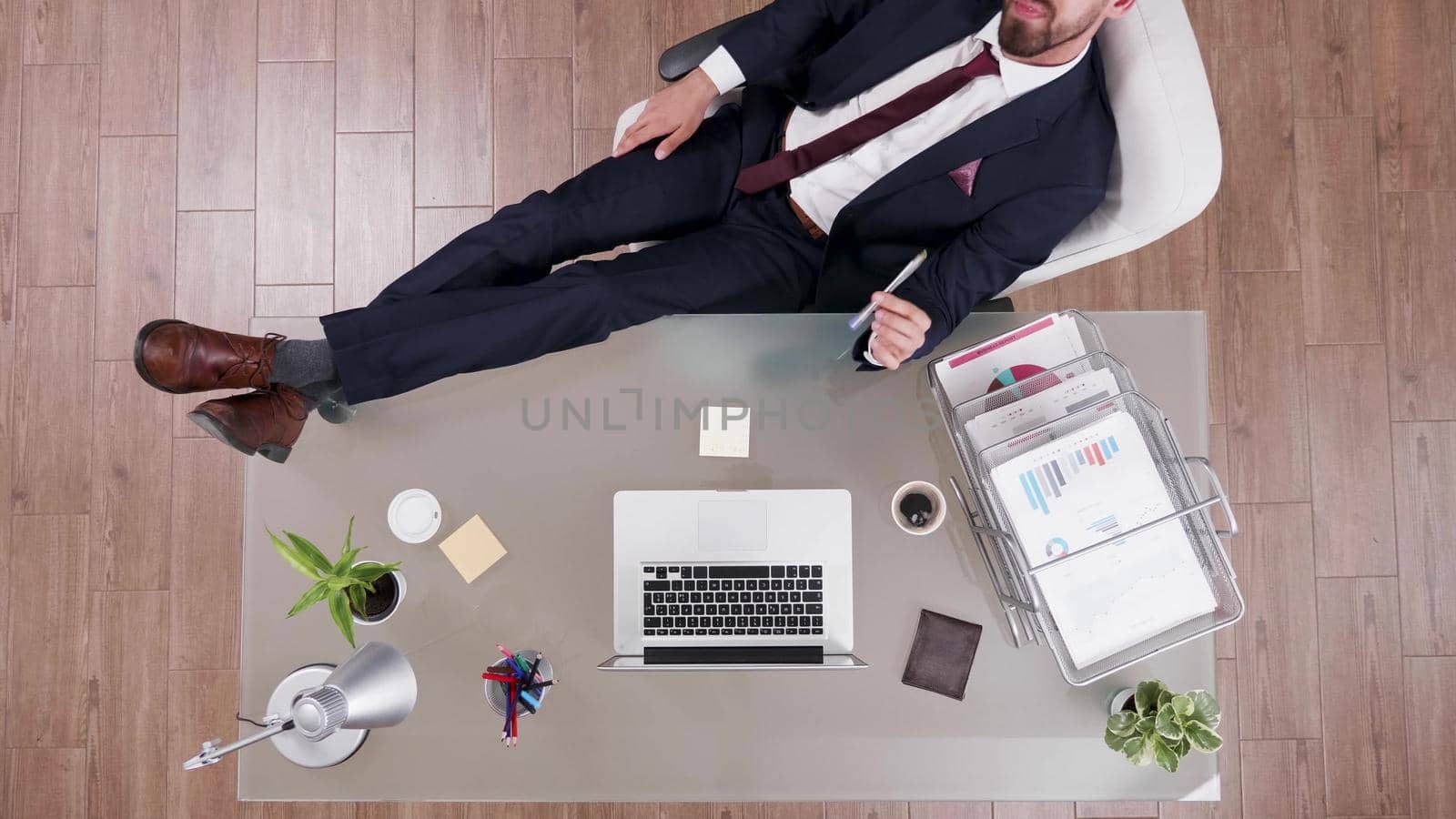 Top view of businessman in suit staying relaxed with feet on office desk thinking at financial profit. Executive manager working in startup company office at management investments