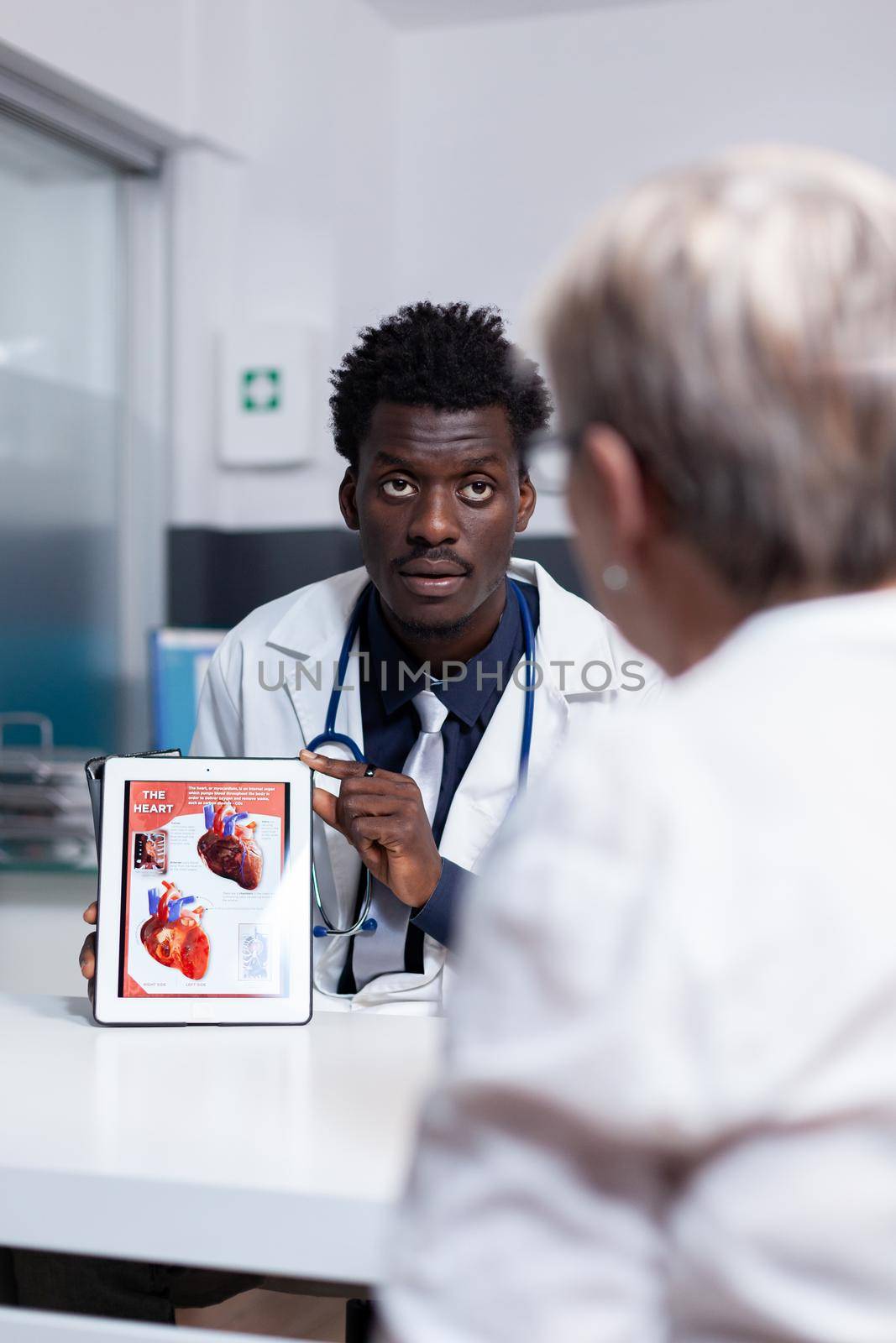 African american man with doctor occupation using tablet showing illustration of organs to old patient for medical diagnosis. Black medic holding digital device for healthcare consultation