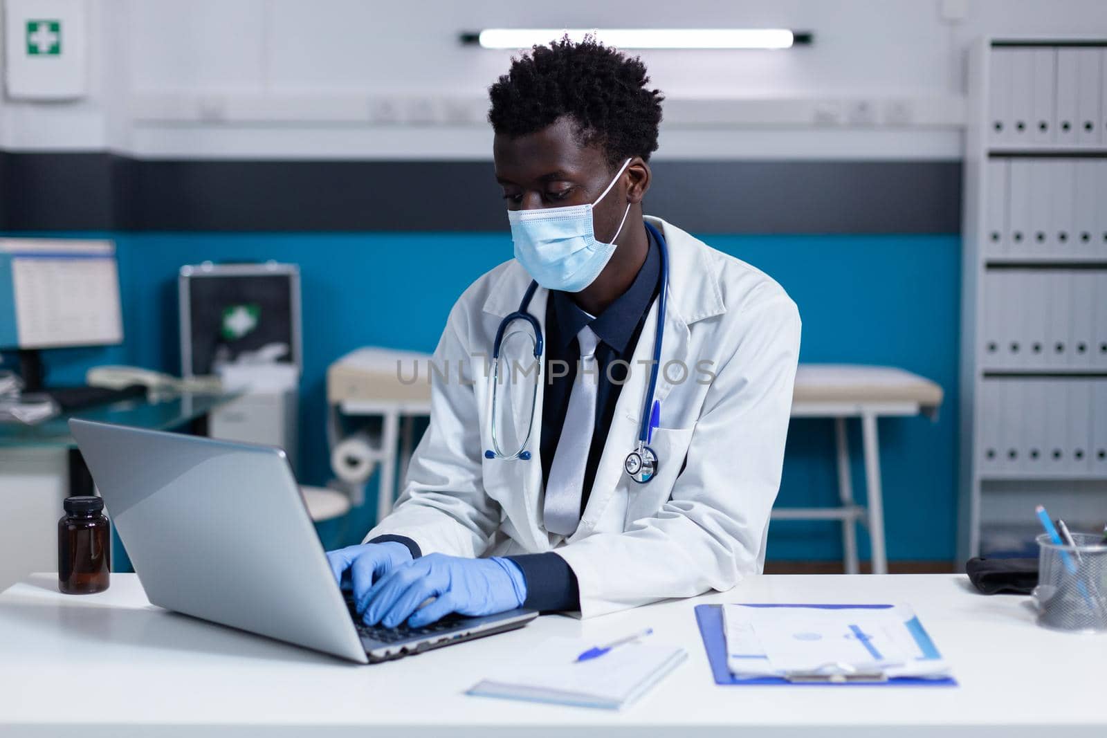 Black man with doctor occupation using laptop on desk by DCStudio