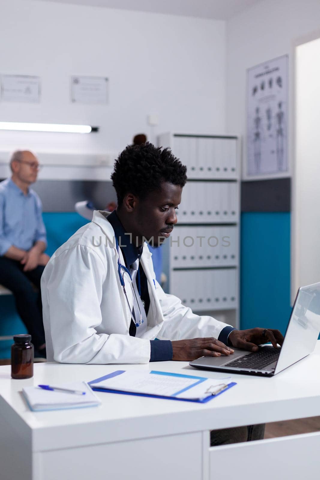 Portrait of african american doctor sitting at desk using laptop by DCStudio