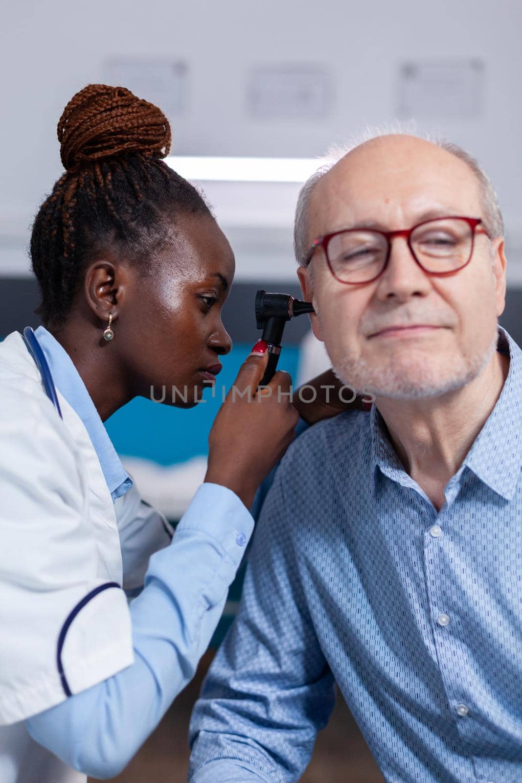 Otologist of african ethnicity consulting elder patient using professional otoscope in healthcare office. Black doctor with metal tool for ear checkup and stethoscope checking on senior man